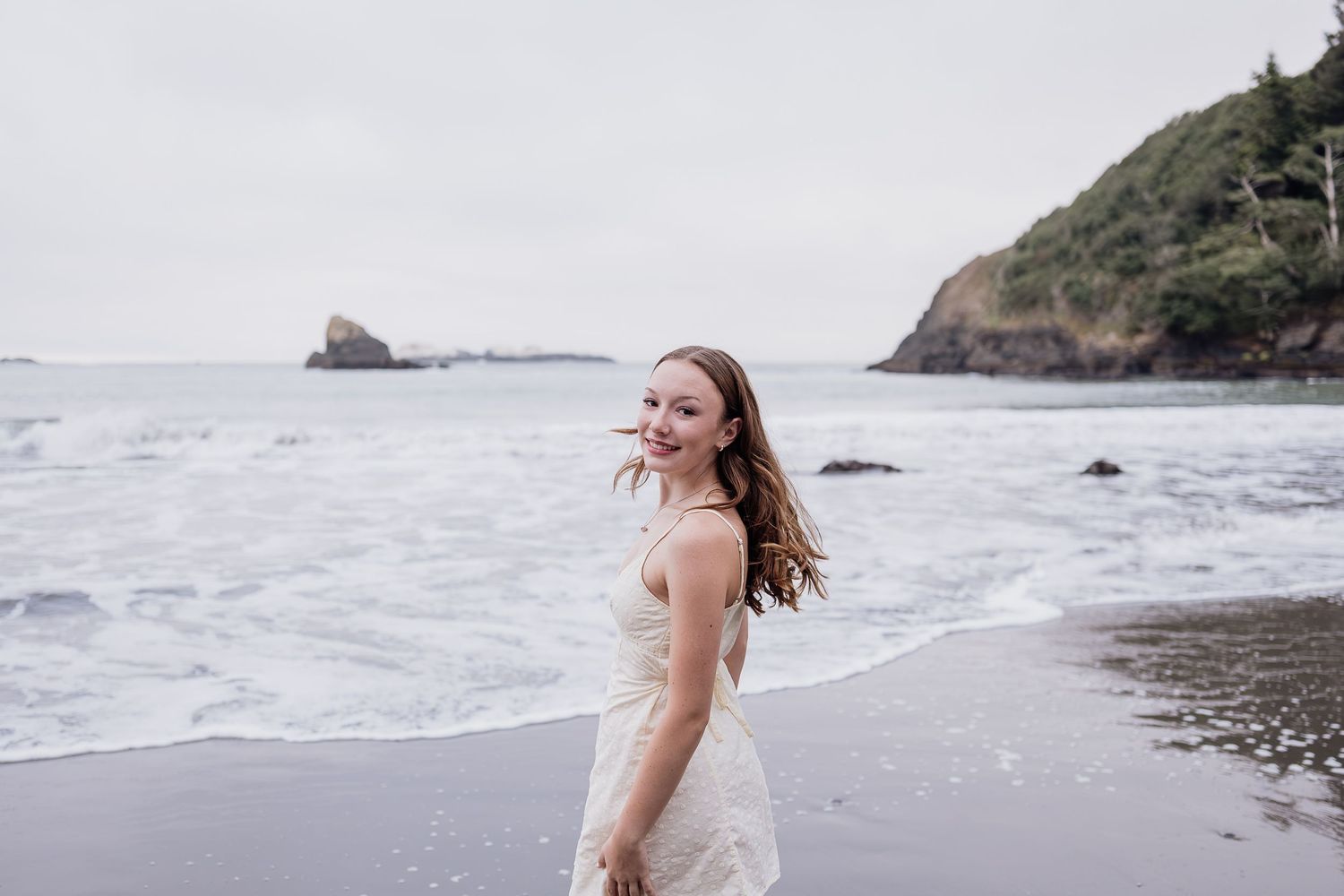 girl smiling turning to smile at the camera s she faces the ocean.