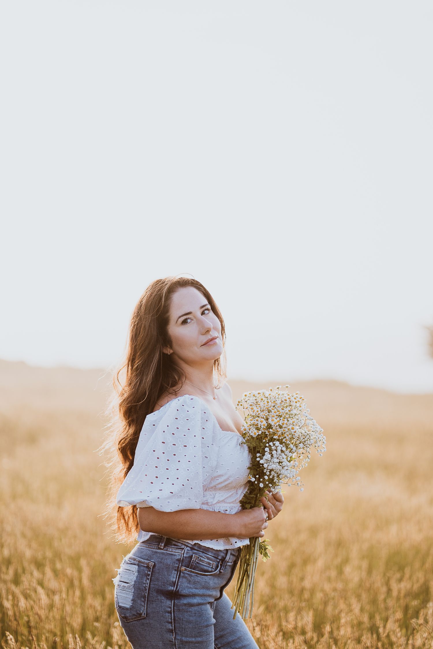 Sunny grassy field, woman in white shirt and jeans holding a bouquet of small flowers
