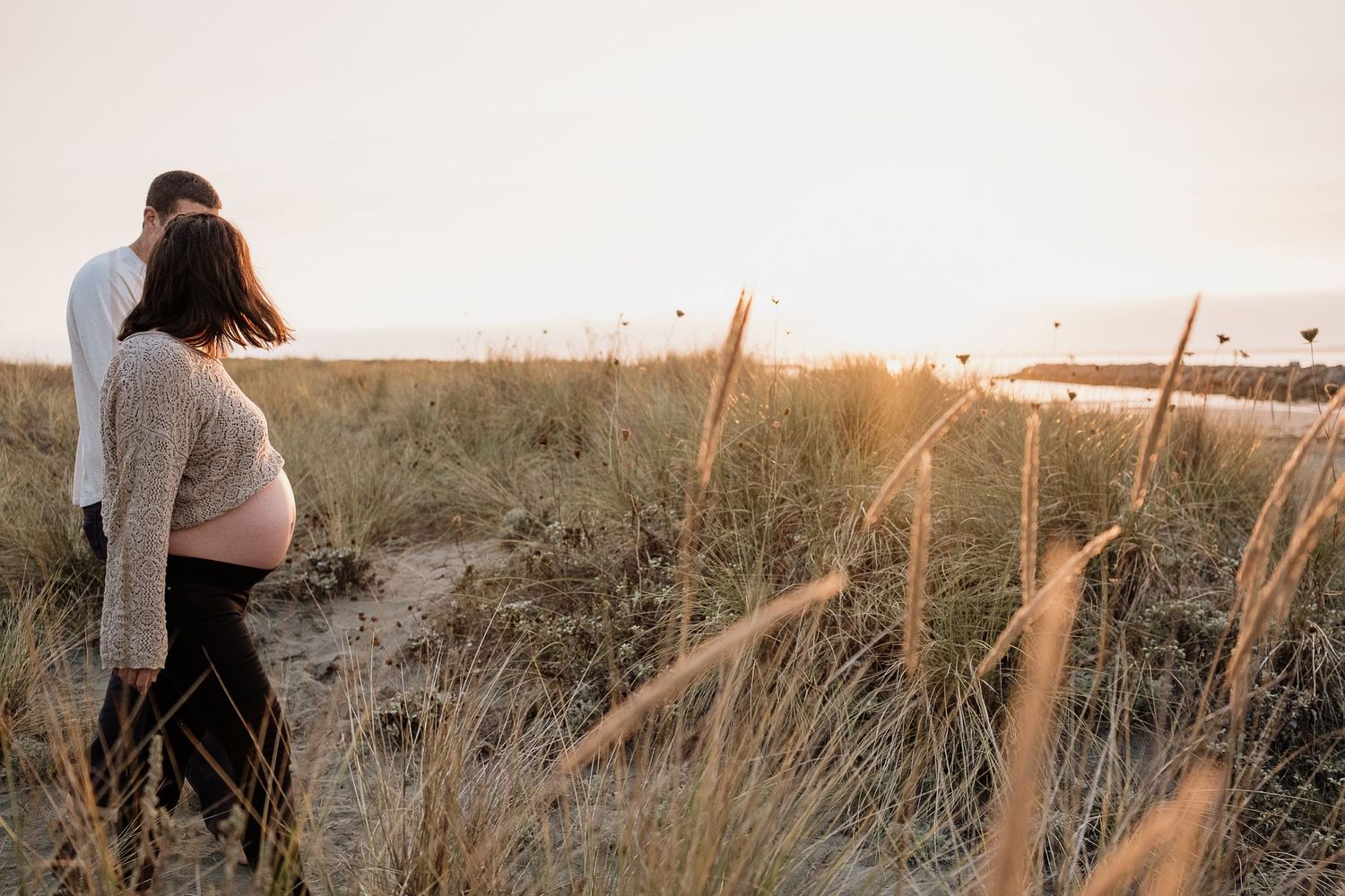 pregnant woman and man holding hands walking at the beach