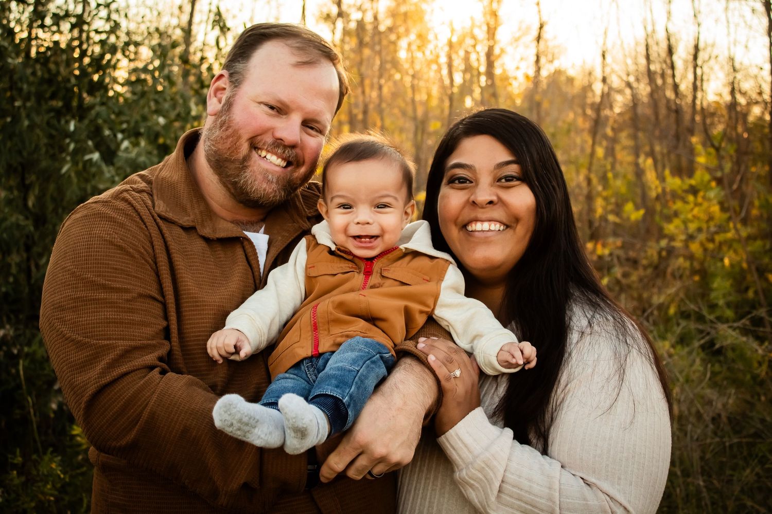 Family portrait session outdoors with autumn trees and golden sunlight.