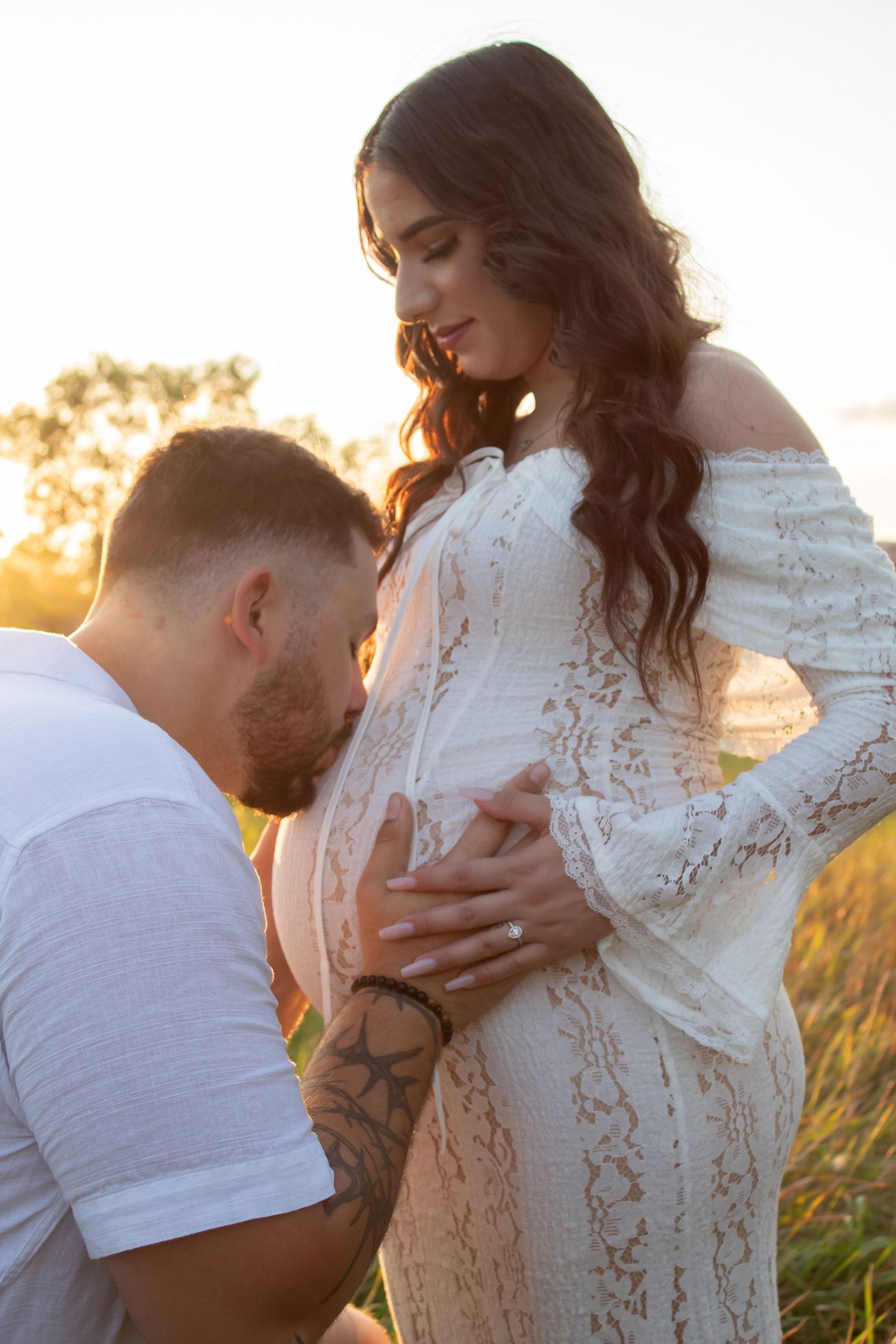 Romantic maternity photoshoot at sunset with couple embracing in a field.