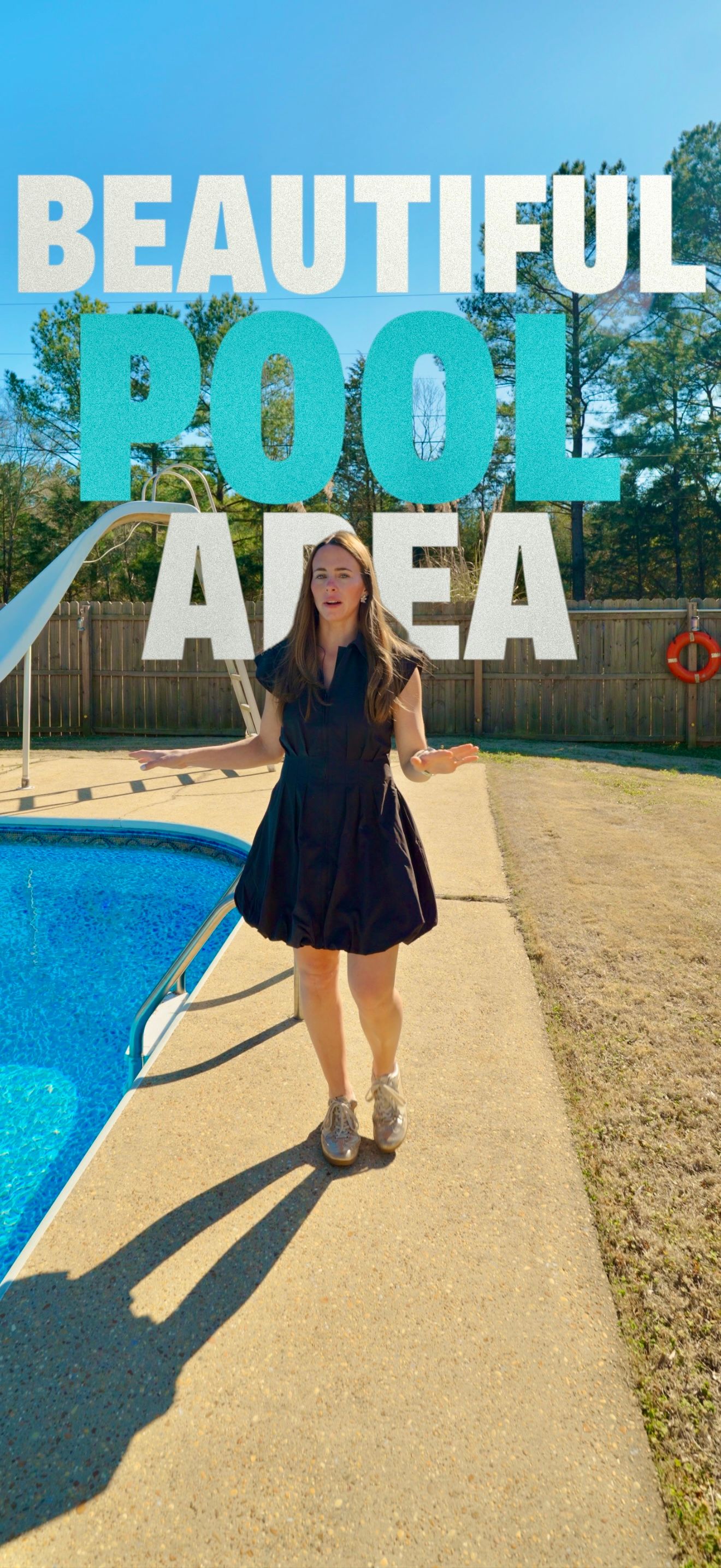 Woman in black dress posing by a beautiful backyard pool area with a slide and safety ring on a sunny day.