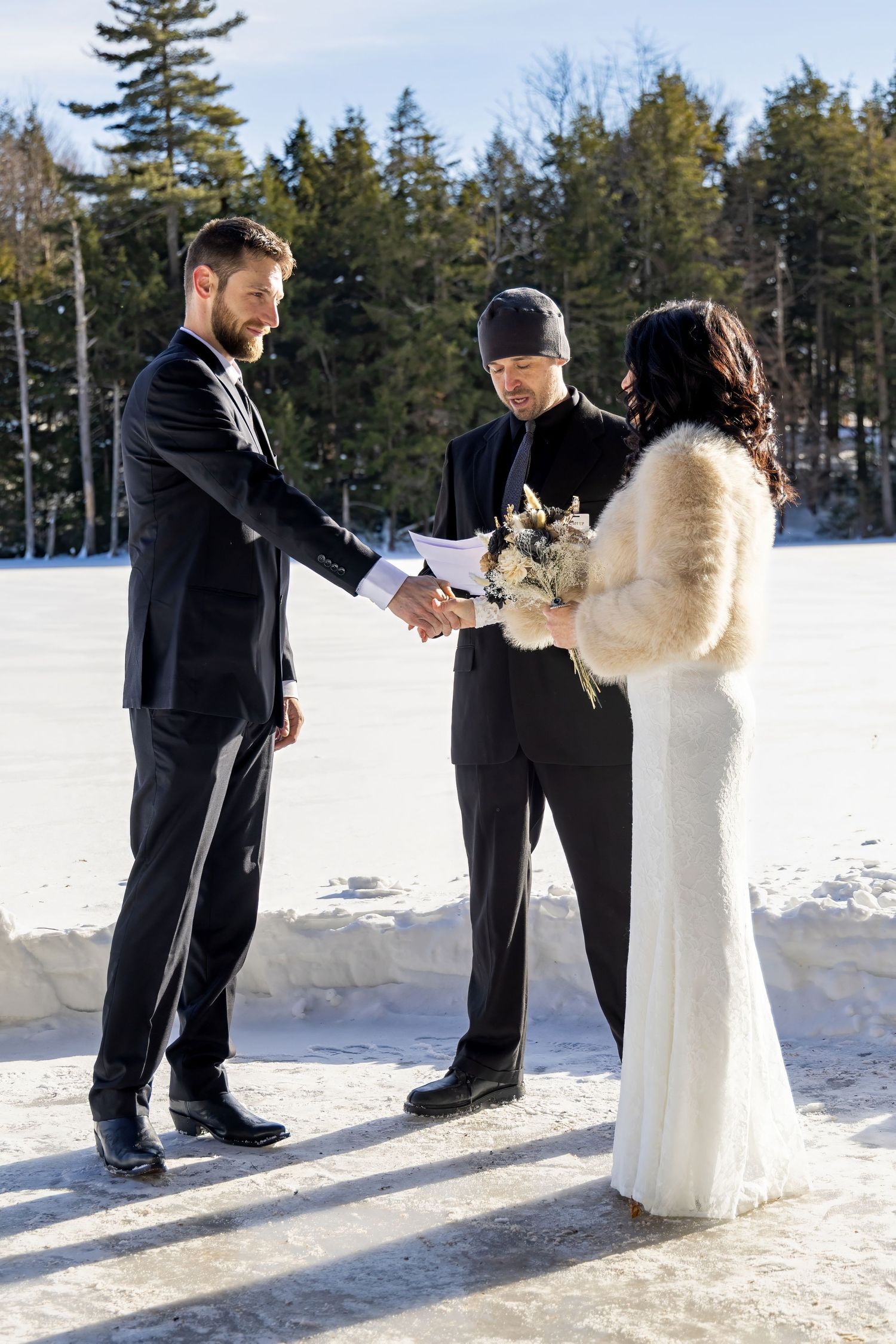 Wedding party poses in formal attire against a snowy winter landscape with pine trees.