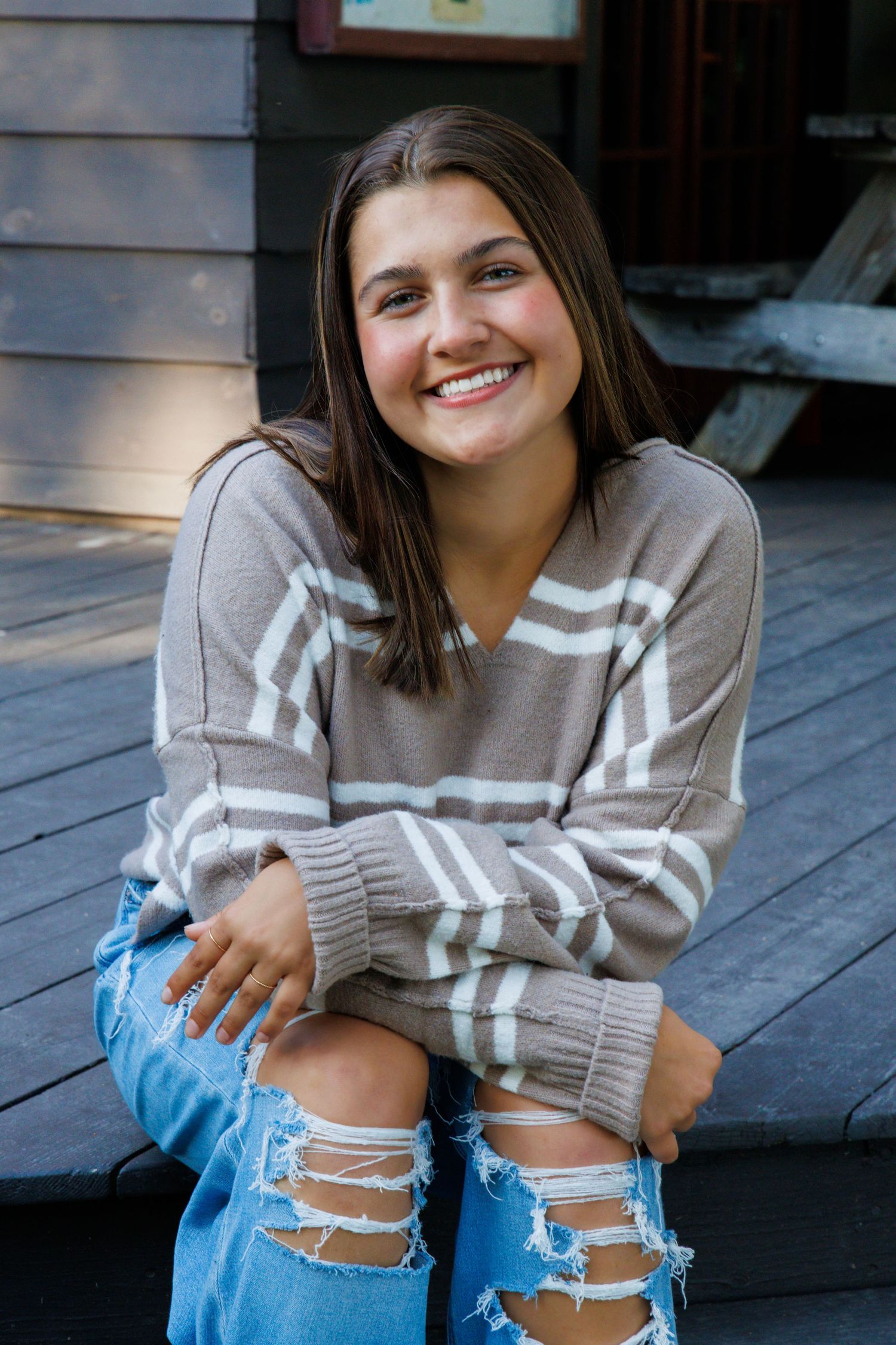 Casual portraits on wooden deck wearing striped sweater and distressed jeans.