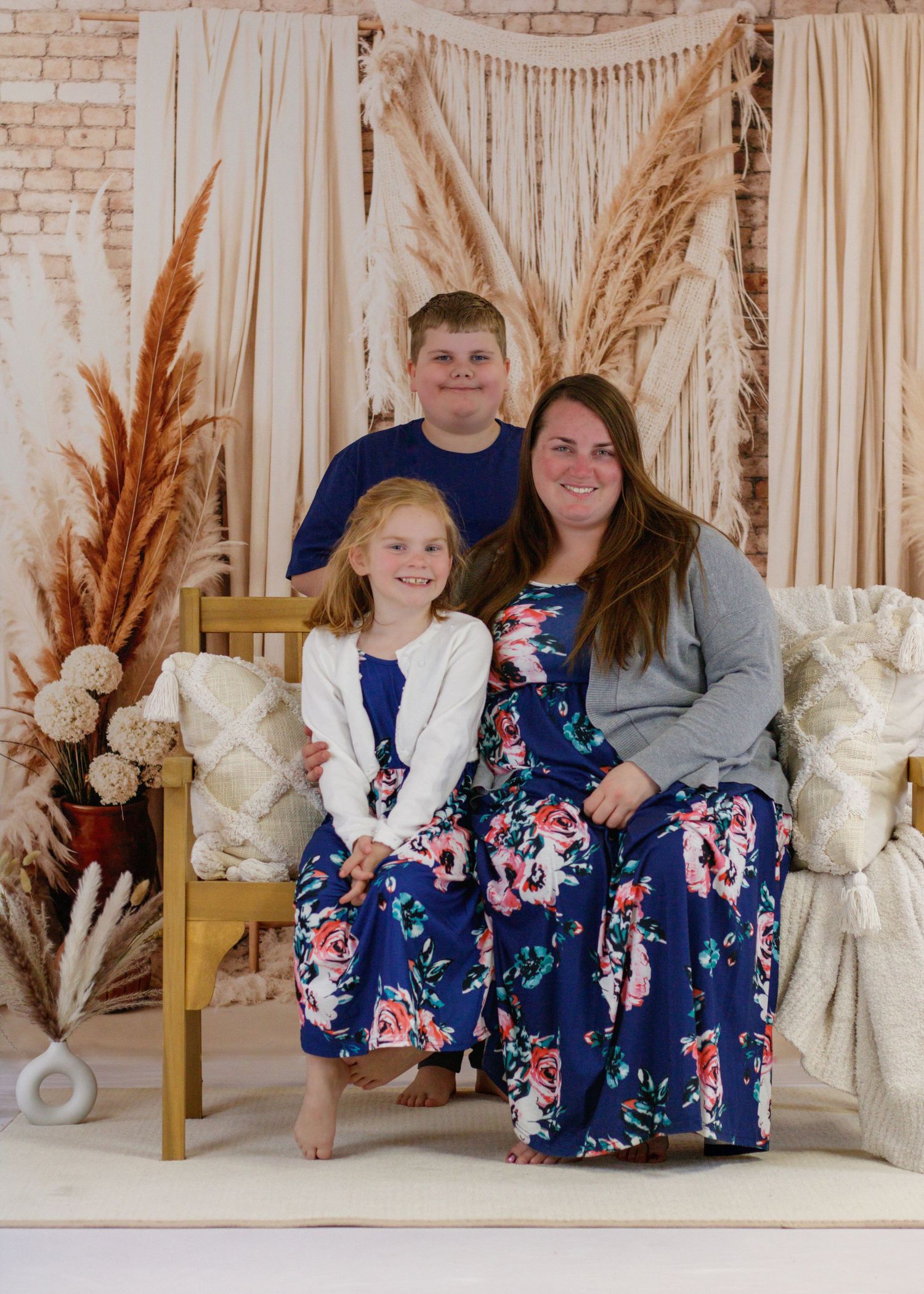 Family portrait with matching floral dresses against cream macrame backdrop with pampas grass.