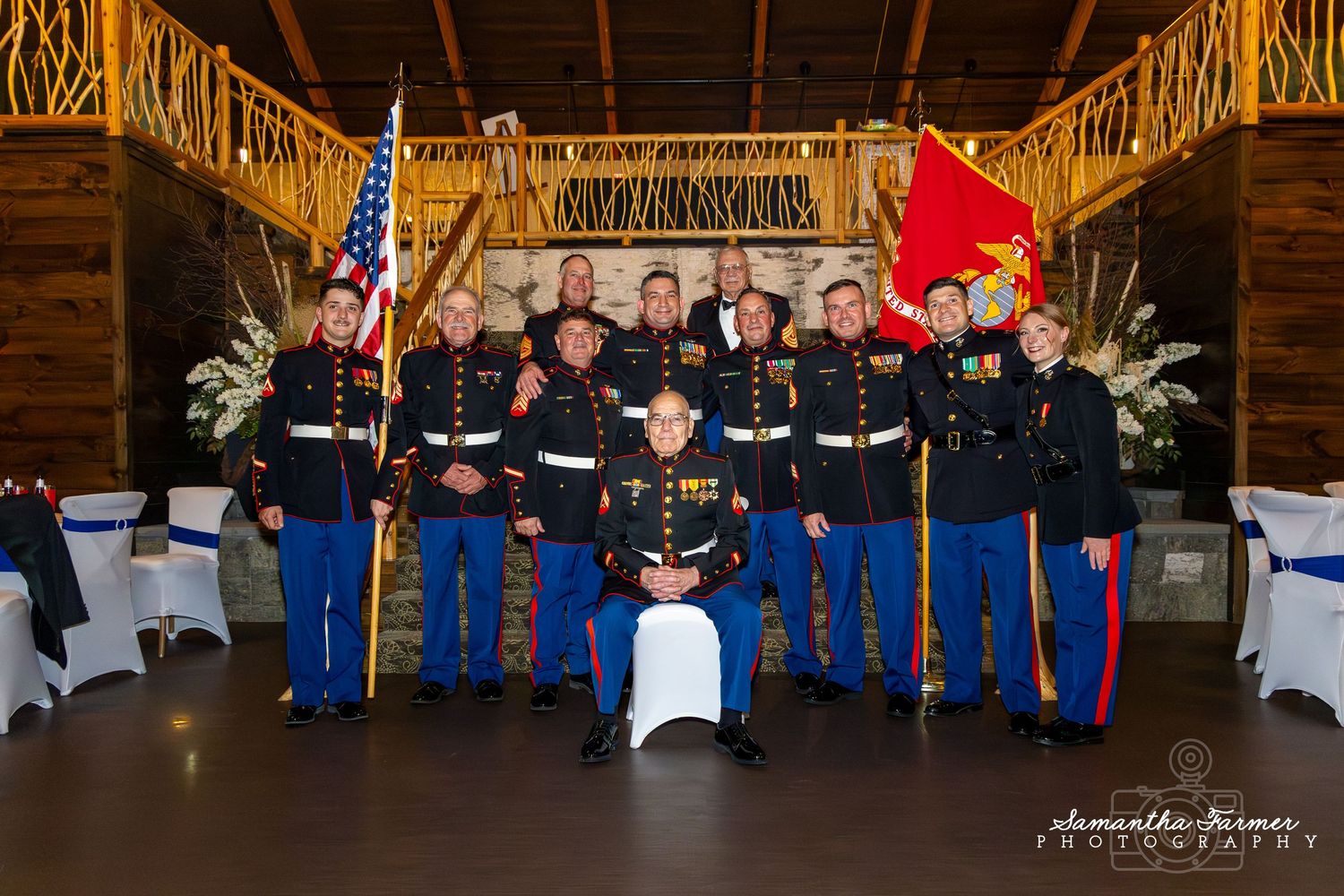 Military service members seated in formal uniforms at a special event with decorative backdrop.