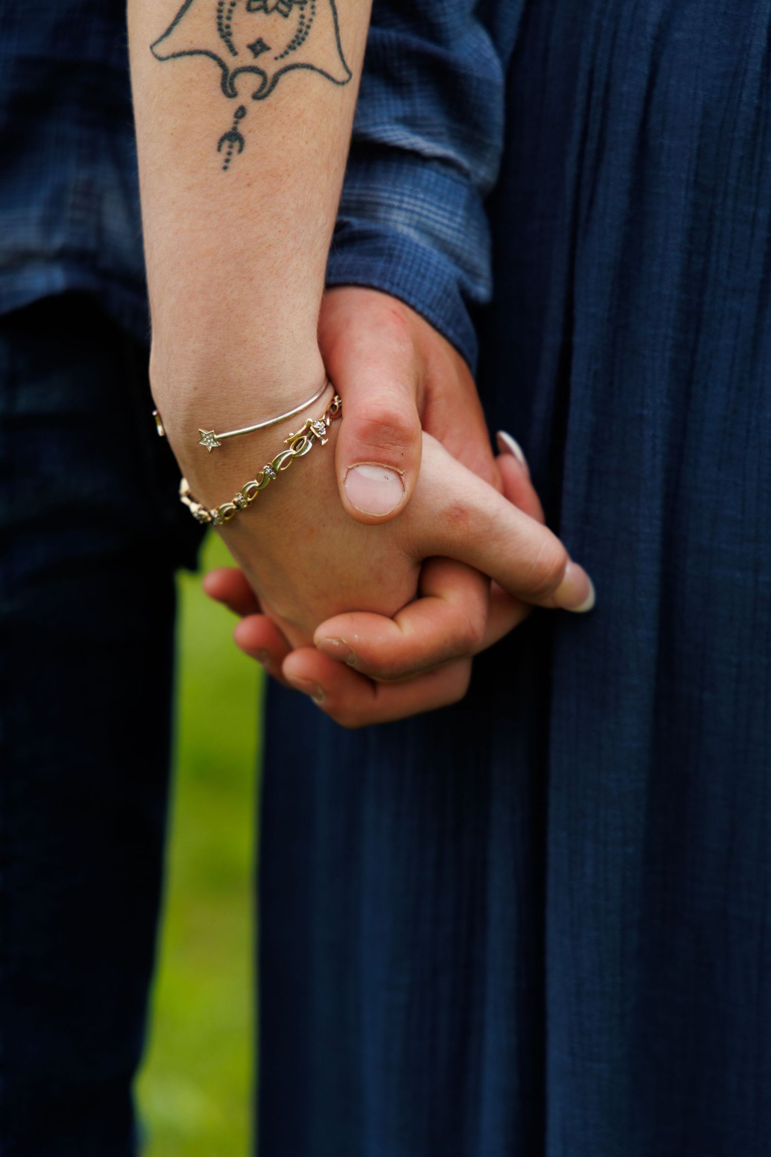 A close-up of clasped hands showing a tattoo and delicate bracelet jewelry.