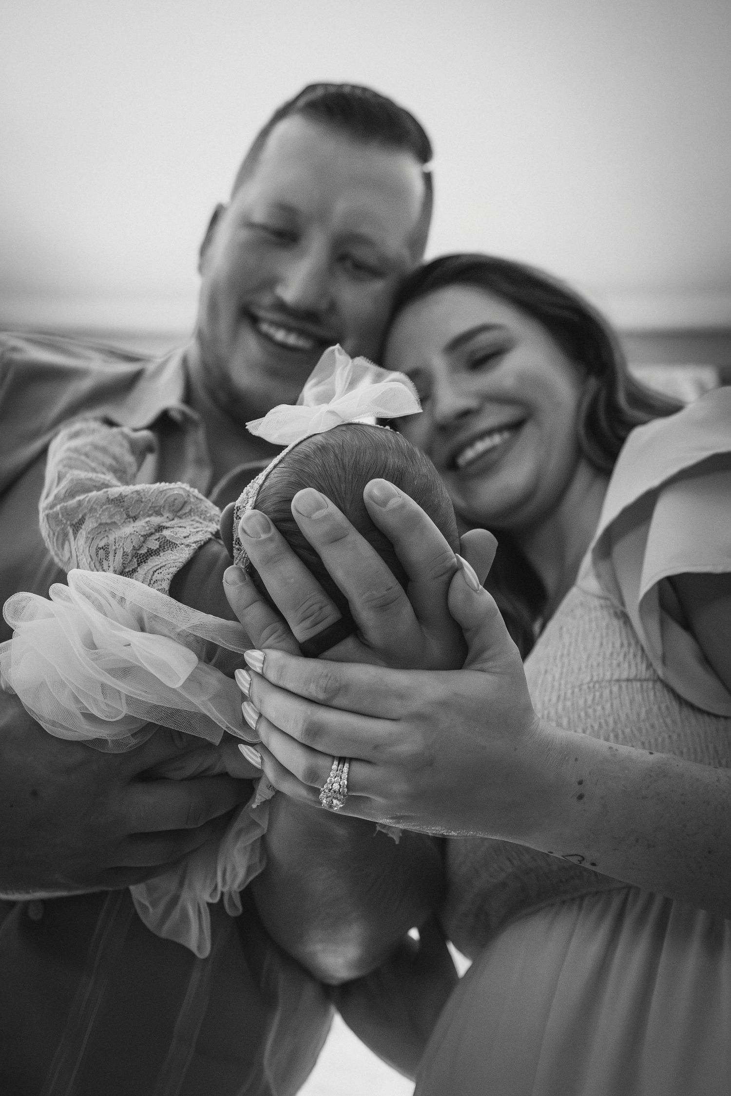 Black and white photo of smiling parents holding their newborn baby with a flower headband.