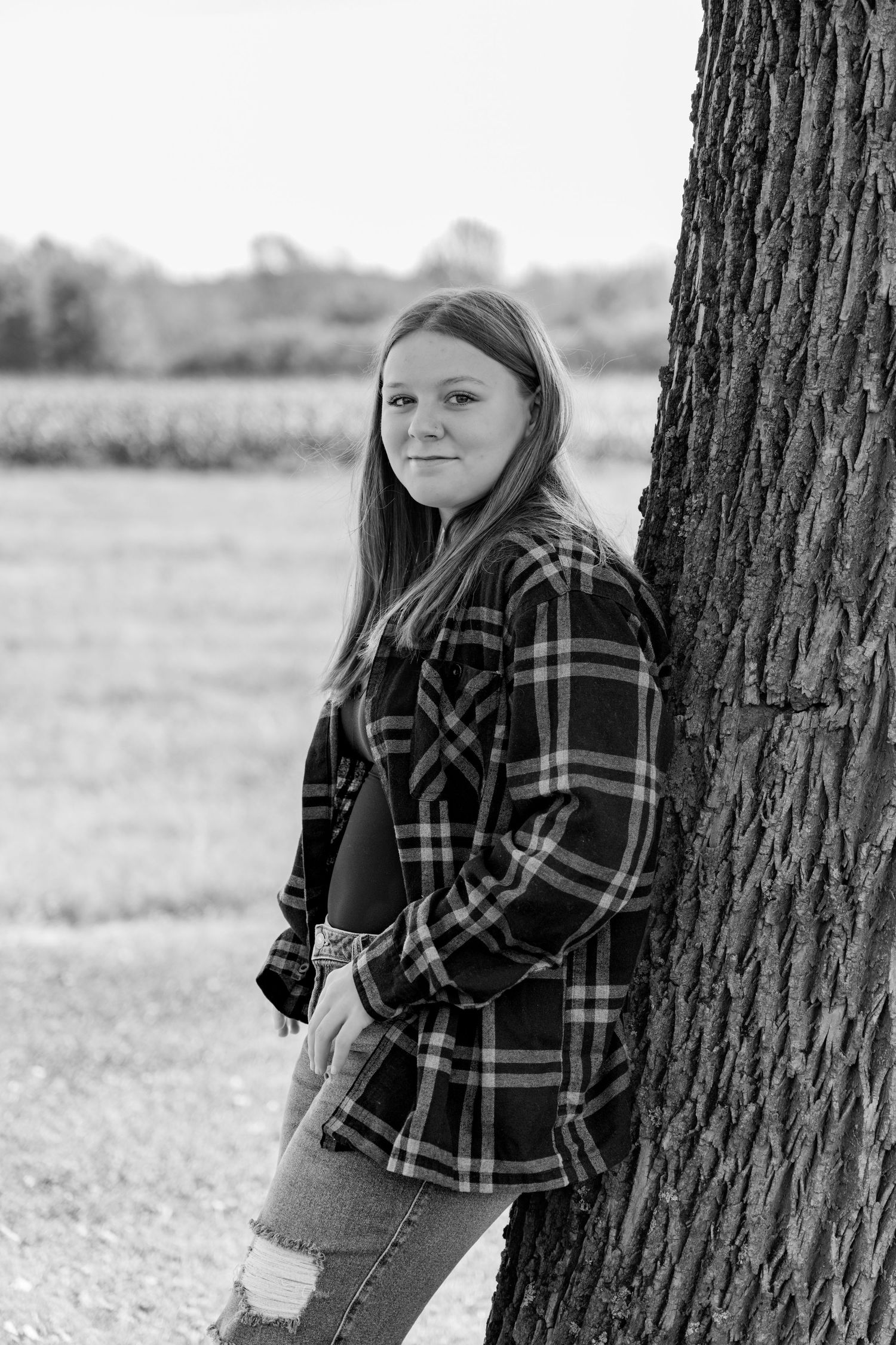Black and white portraits in plaid flannel leaning against tree trunk.