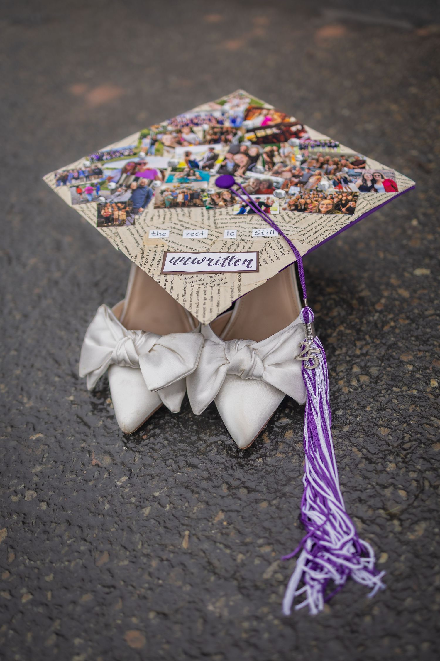 Close-up of a decorated graduation cap with white bows and purple tassel lying on asphalt.