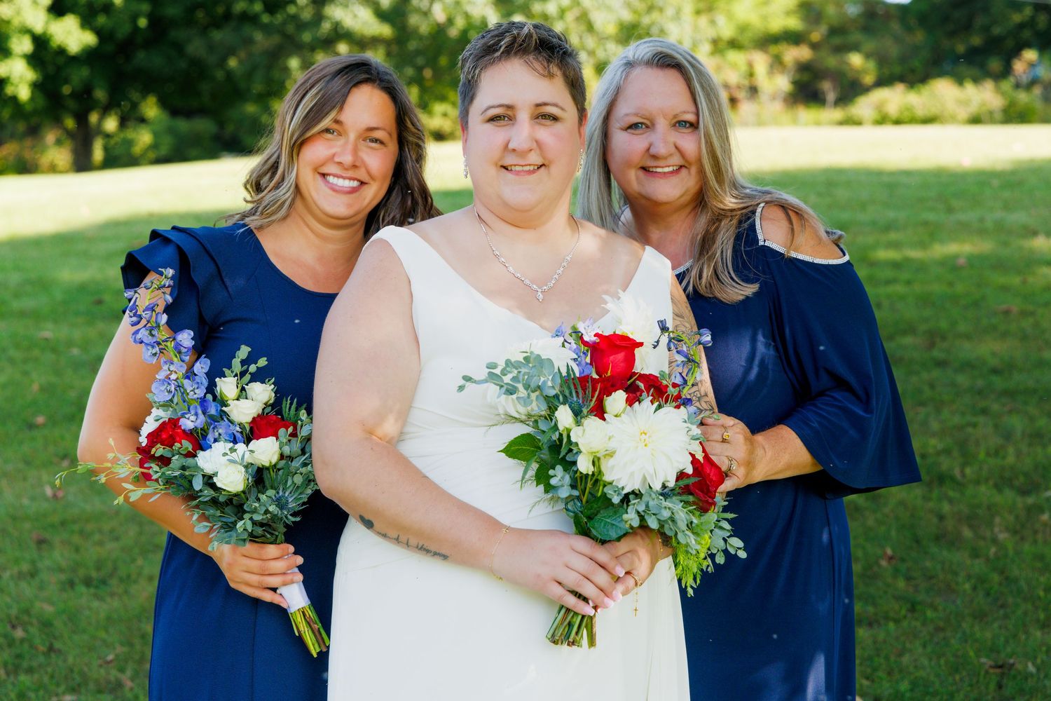 Wedding party poses outdoors in navy blue and white attire with colorful bouquets.
