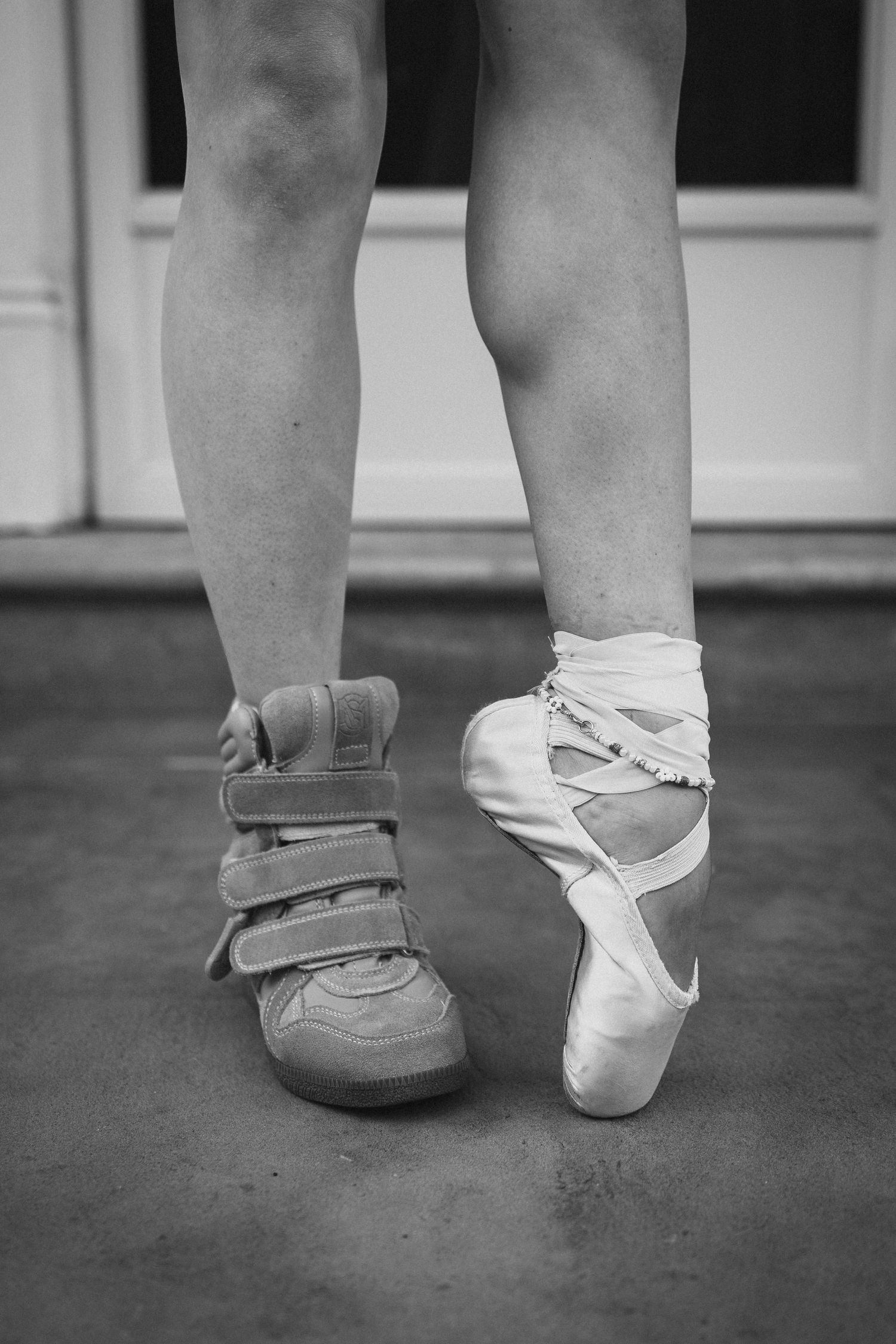 Black and white photo of legs wearing one sneaker and one ballet pointe shoe, contrasting dance styles.