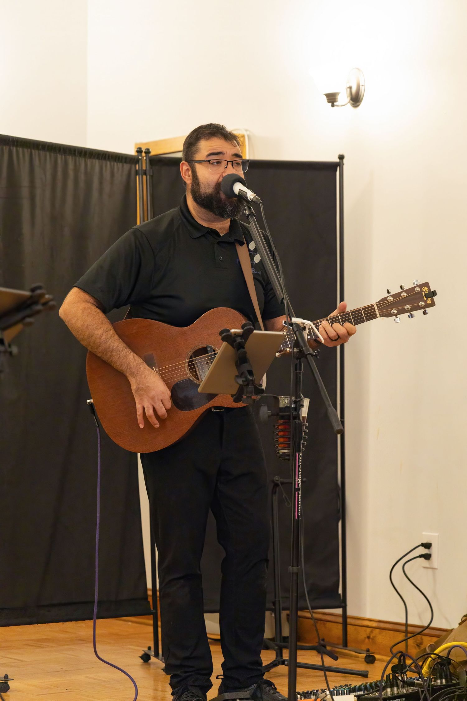 Musician performing with acoustic guitar on stage against black backdrop.