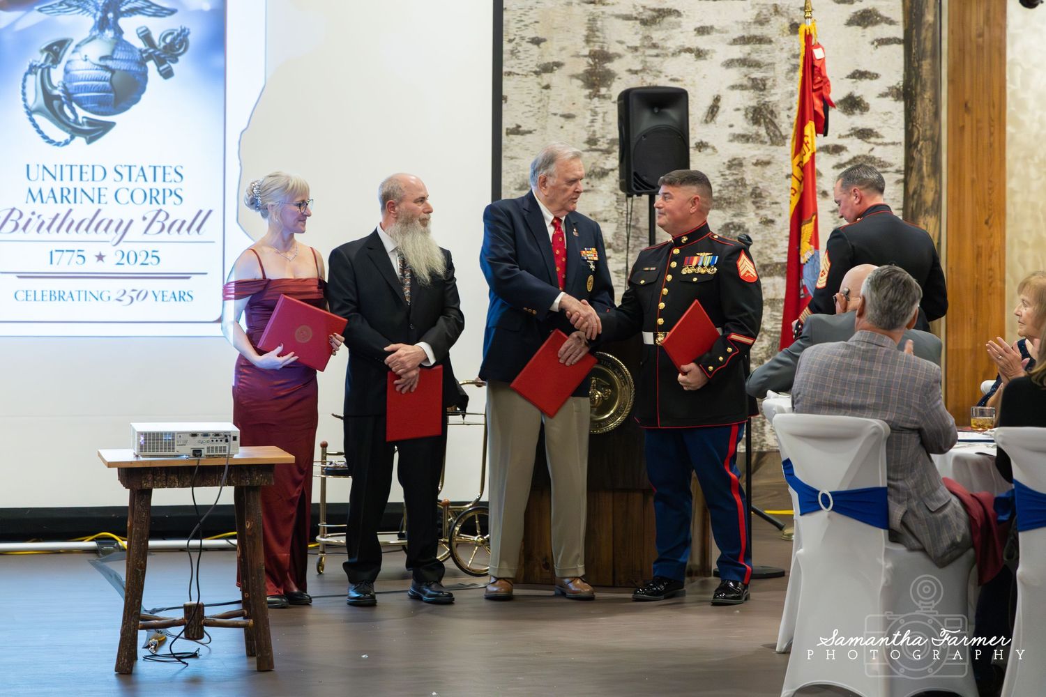 Military ceremonial event setup in a banquet hall with stone walls and projector screen.