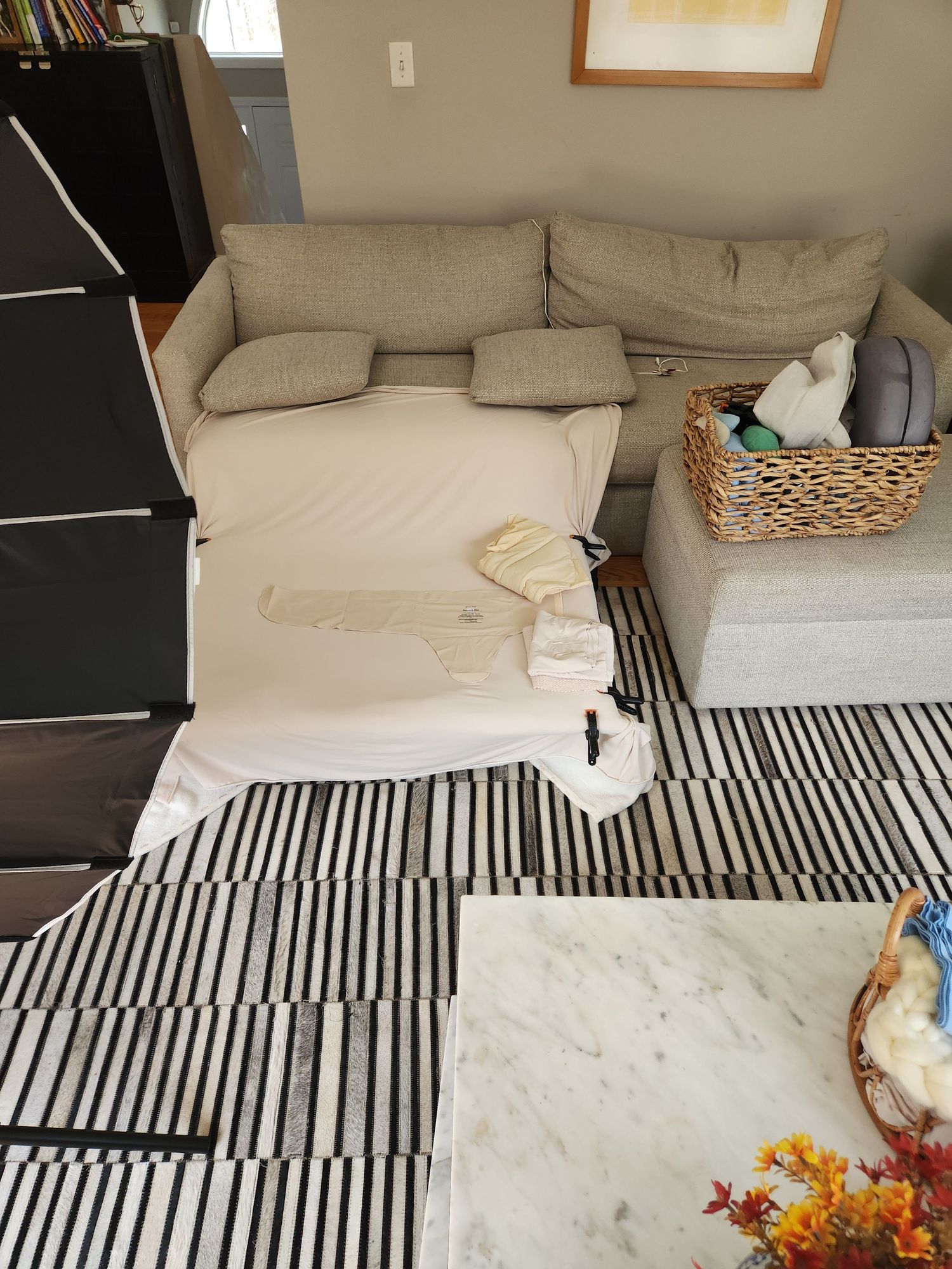 Beige sectional sofa with white bedding on a black and white striped rug next to a marble coffee table in a living room.