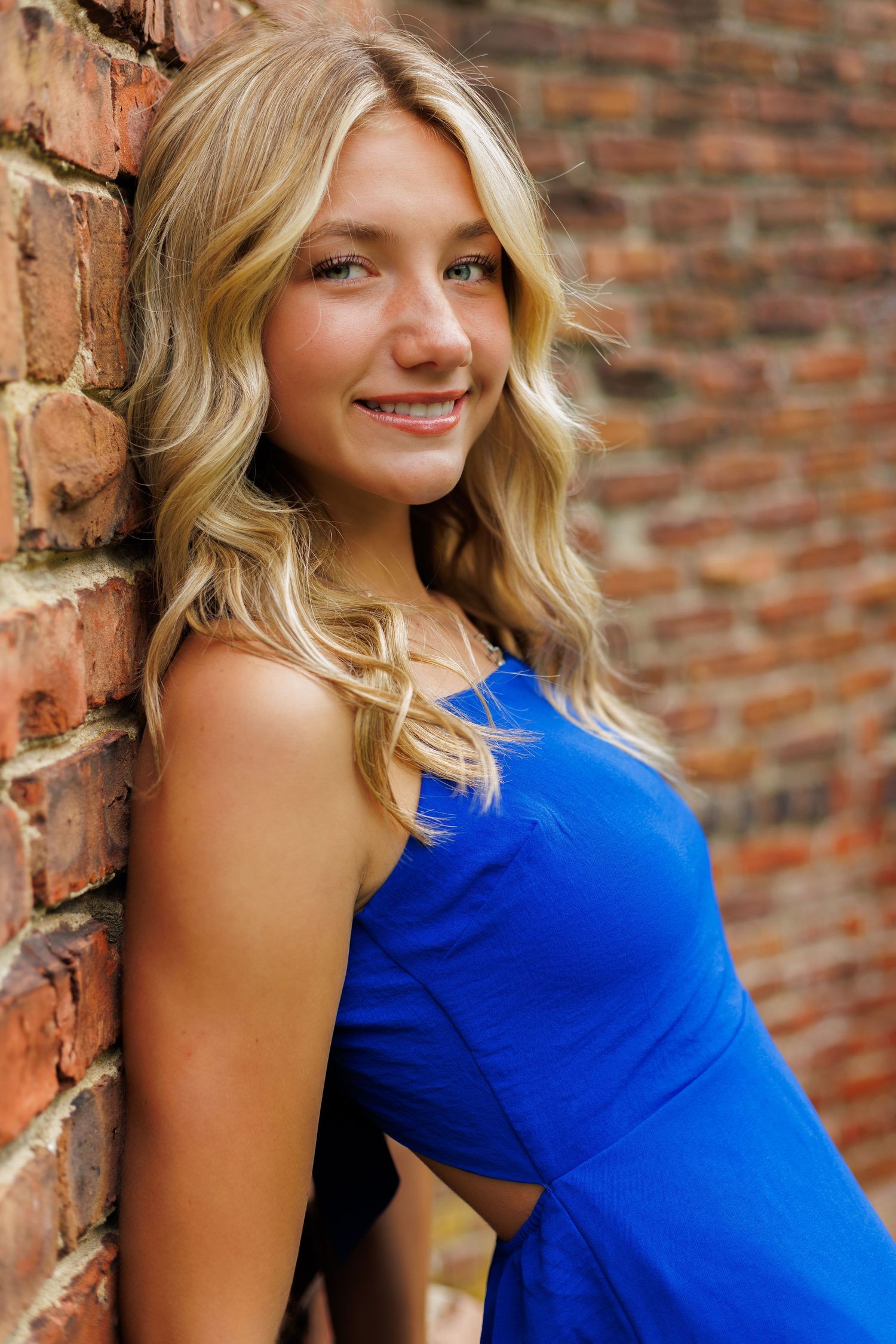 Senior portrait against rustic brick wall wearing bright blue dress.