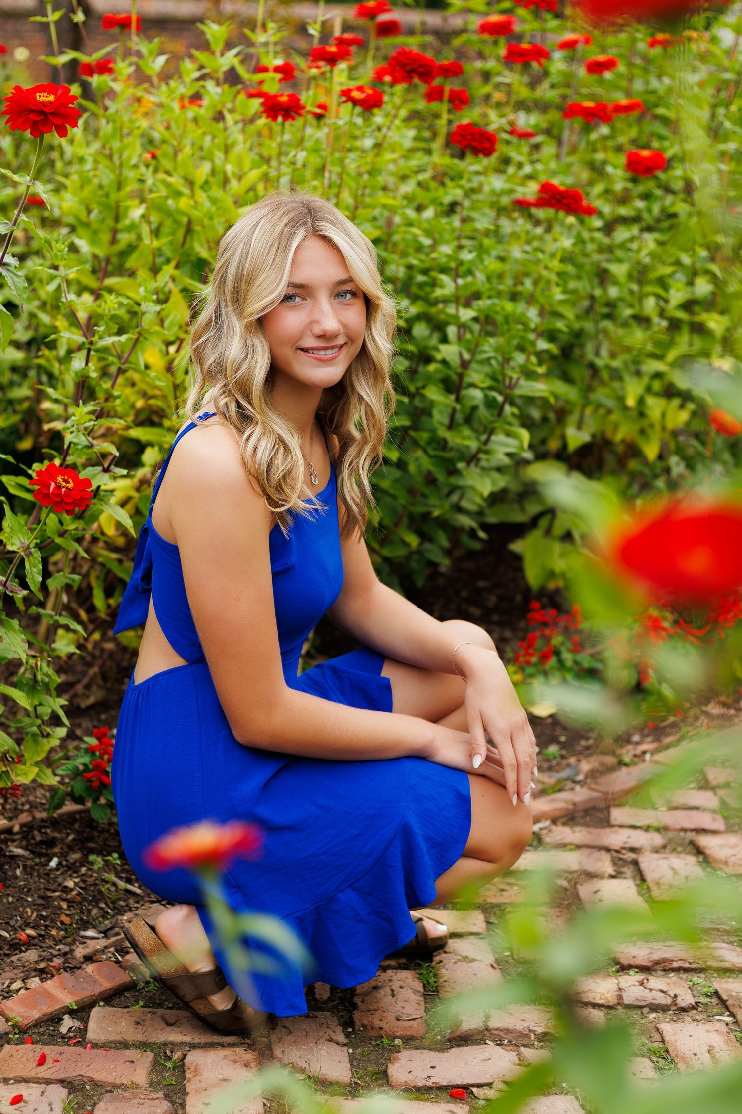 Portraits in a garden setting with bright red flowers and blue dress against stone pathway.