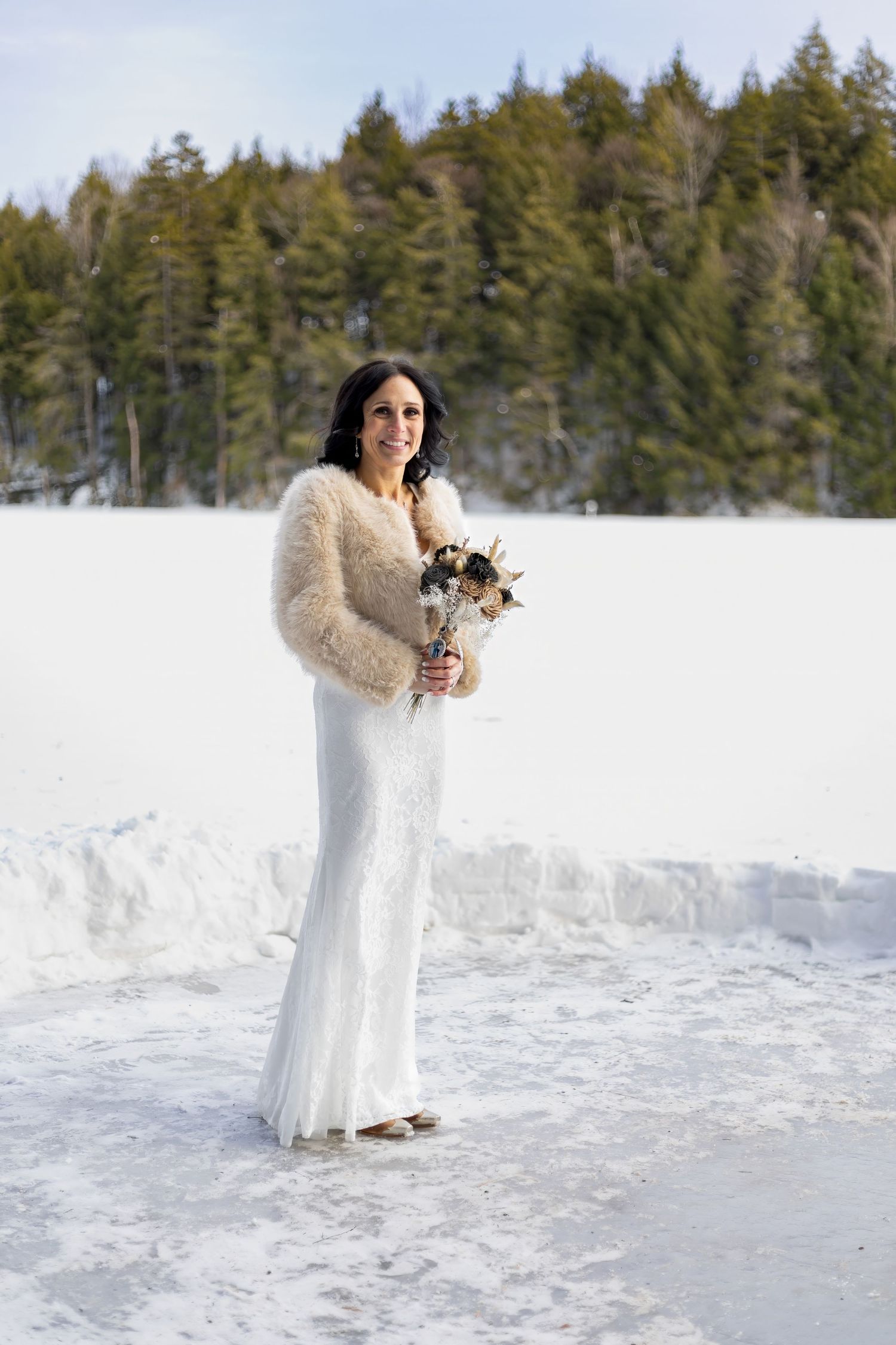 Bride in winter wedding dress poses against snowy forest landscape.