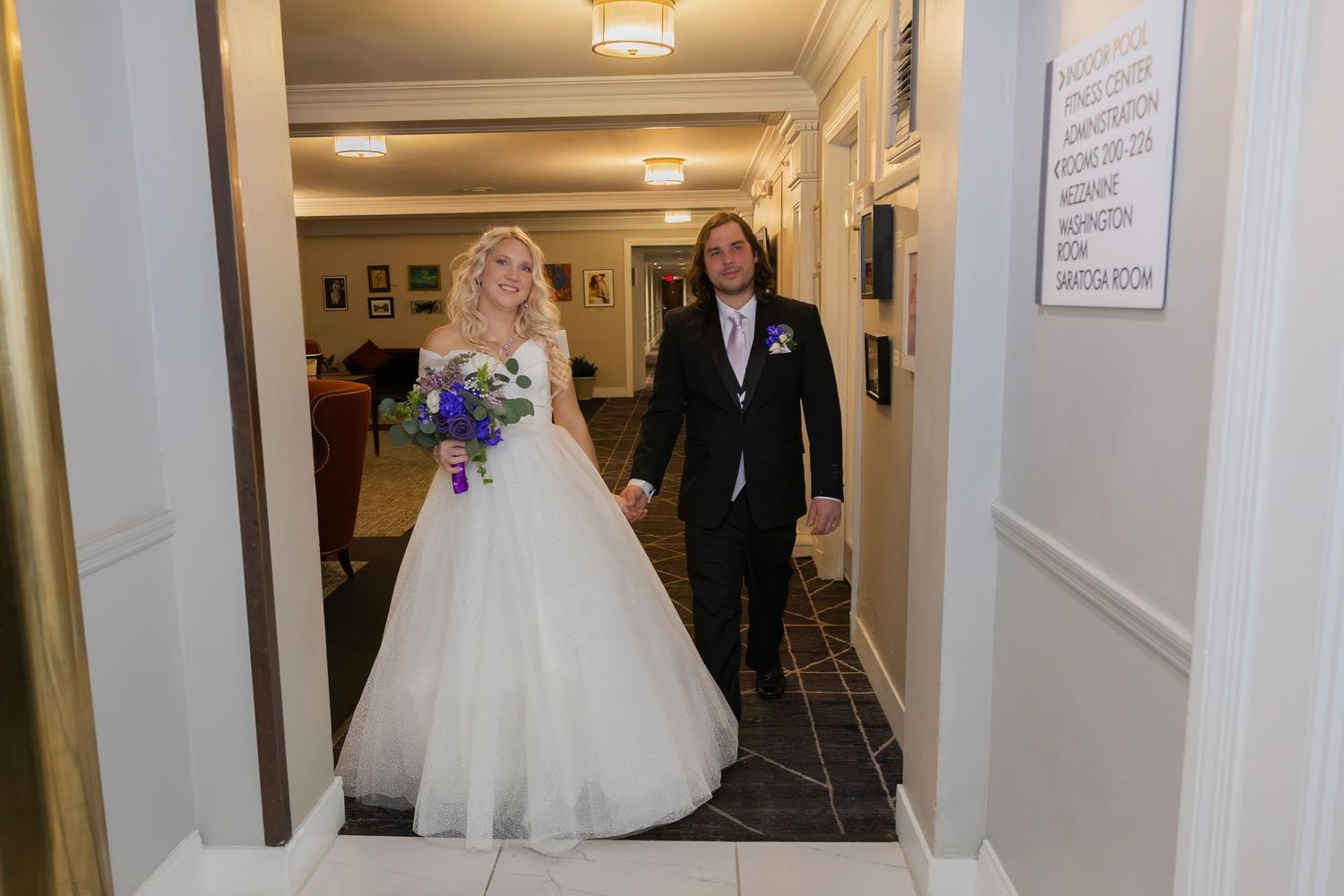 A couple walks down a brightly lit hallway during their wedding celebration.