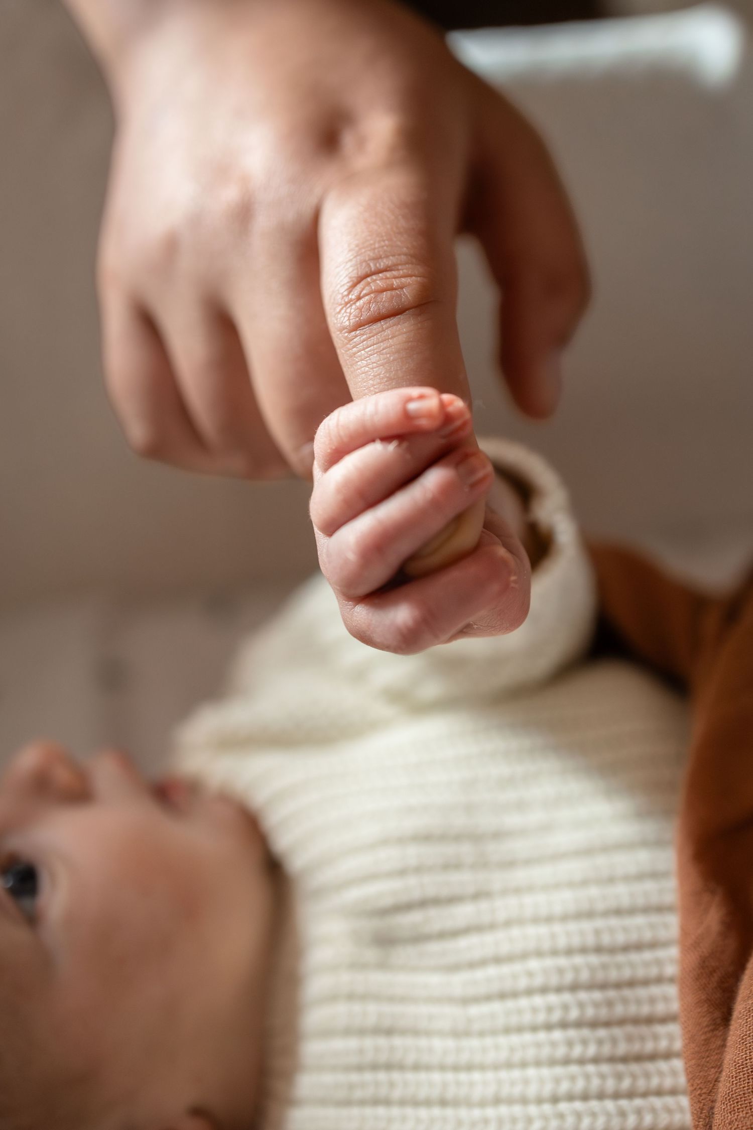 Newborn baby grasping adult finger, close-up of tiny infant hand holding parent finger in tender moment.