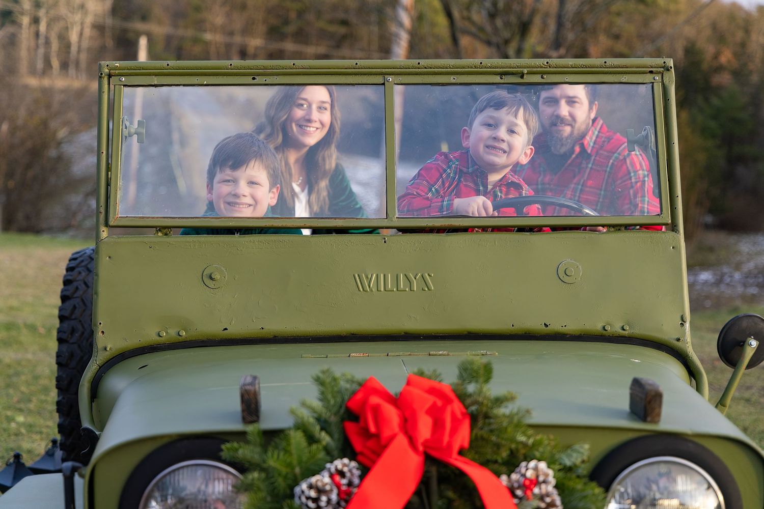 Family riding in vintage military green Jeep decorated with red bow.