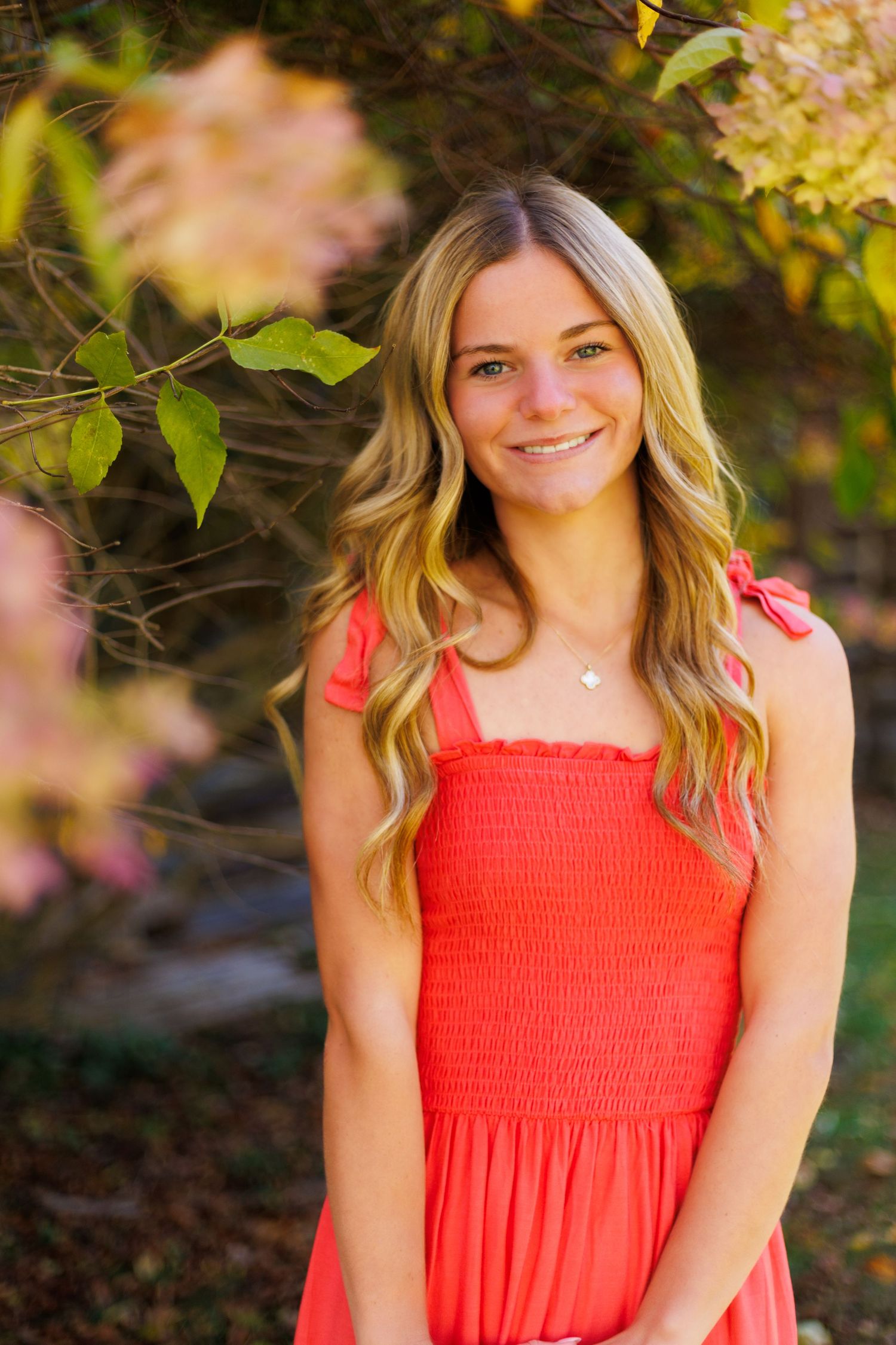 Summer portraits in a coral smocked dress against a leafy natural backdrop.
