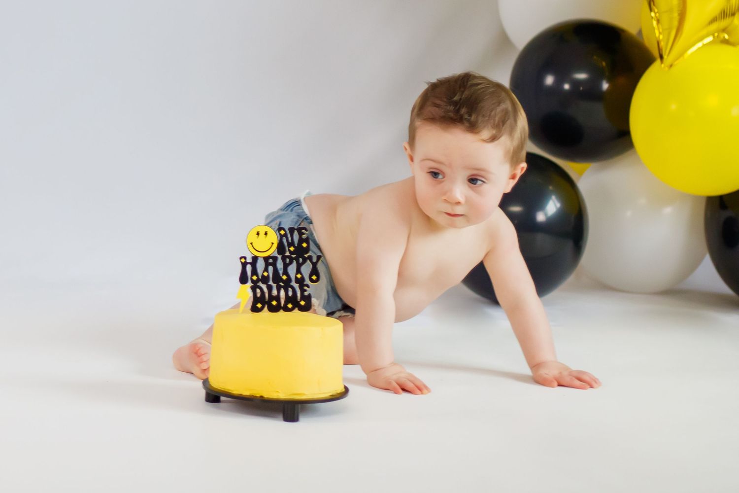 Birthday cake smash photo session with yellow and black balloons and decorations.