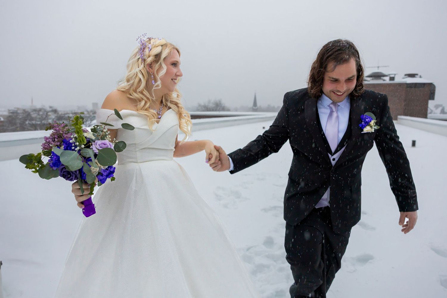 A couple playfully runs through the snow holding bouquets during a winter wedding photoshoot.