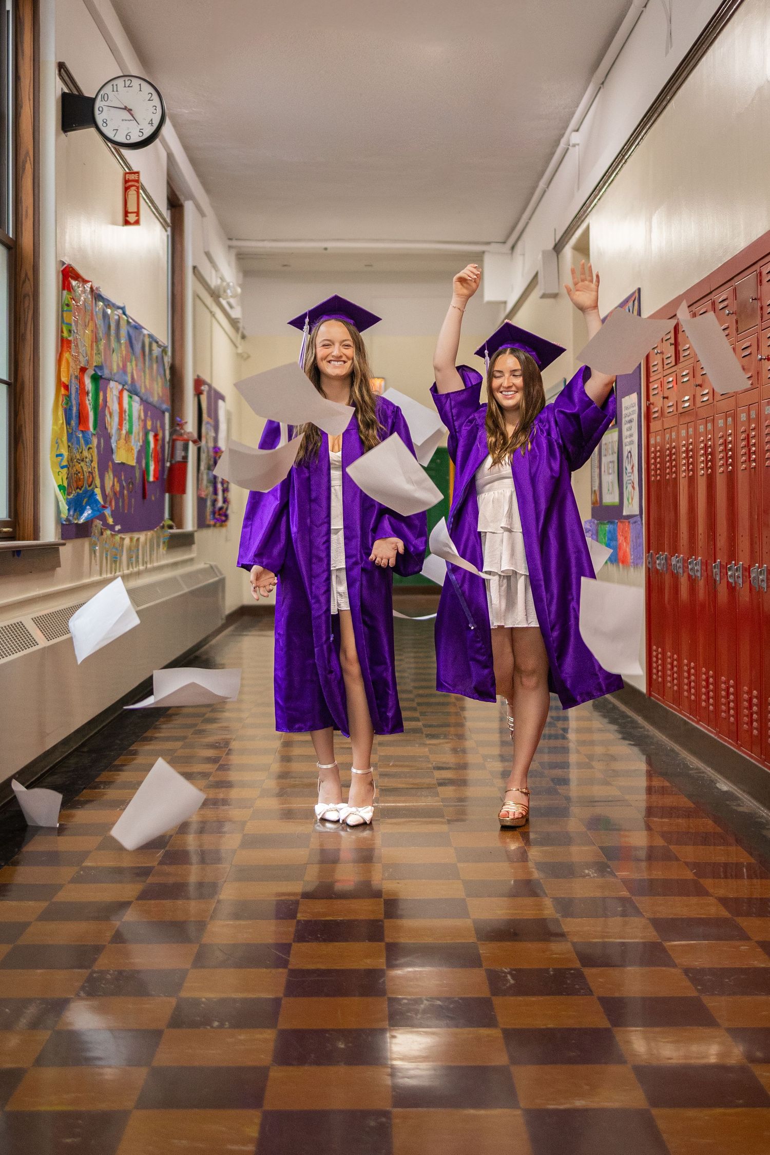 Graduates in purple gowns celebrate in school hallway with lockers.