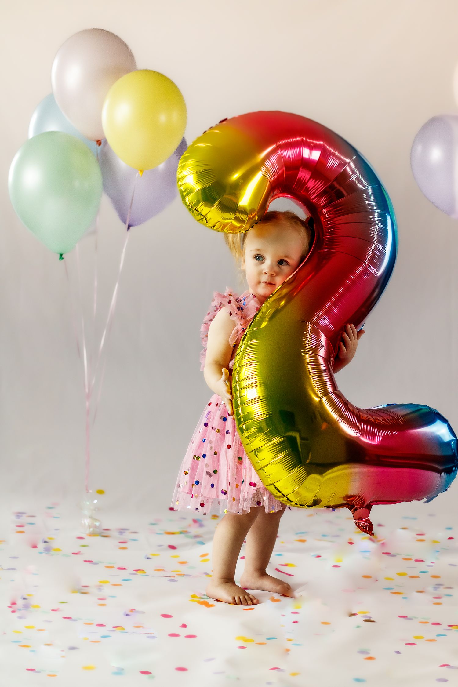 Child in pink dress playing with number 2 balloon and colorful party decorations.