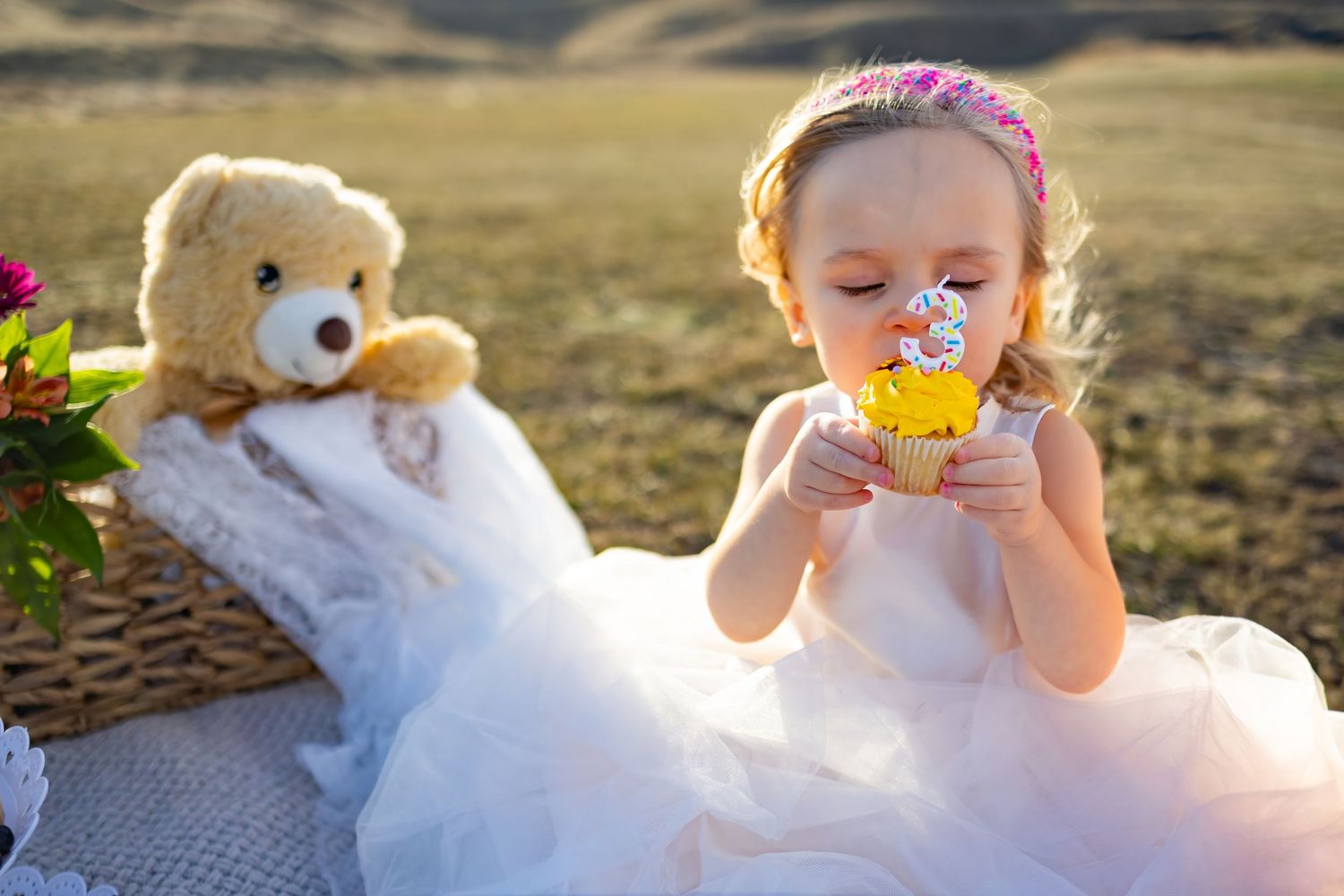 Toddler in white dress playing with cupcake props during sunset photoshoot.