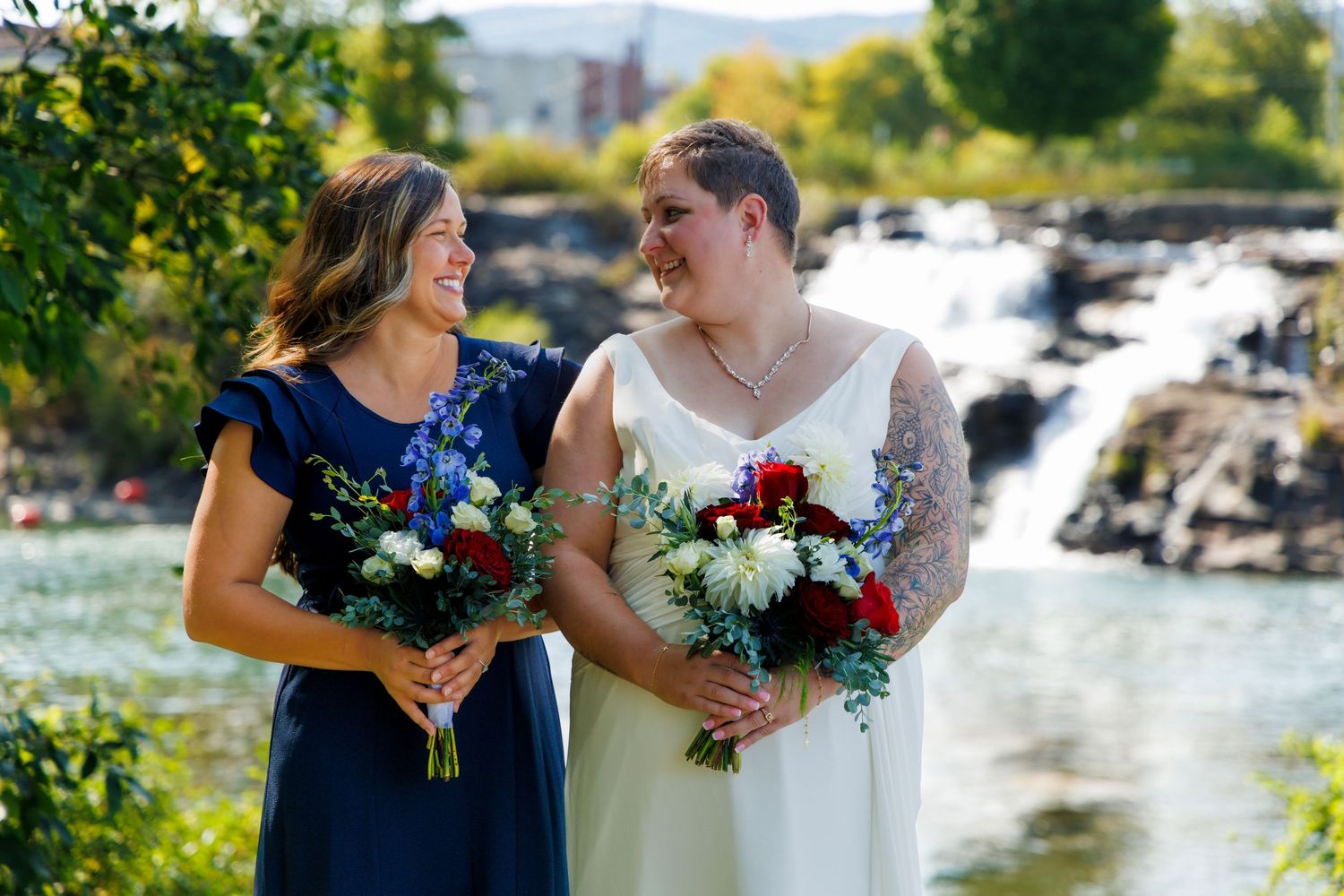 Wedding party members gather by a waterfront location holding vibrant bouquets.