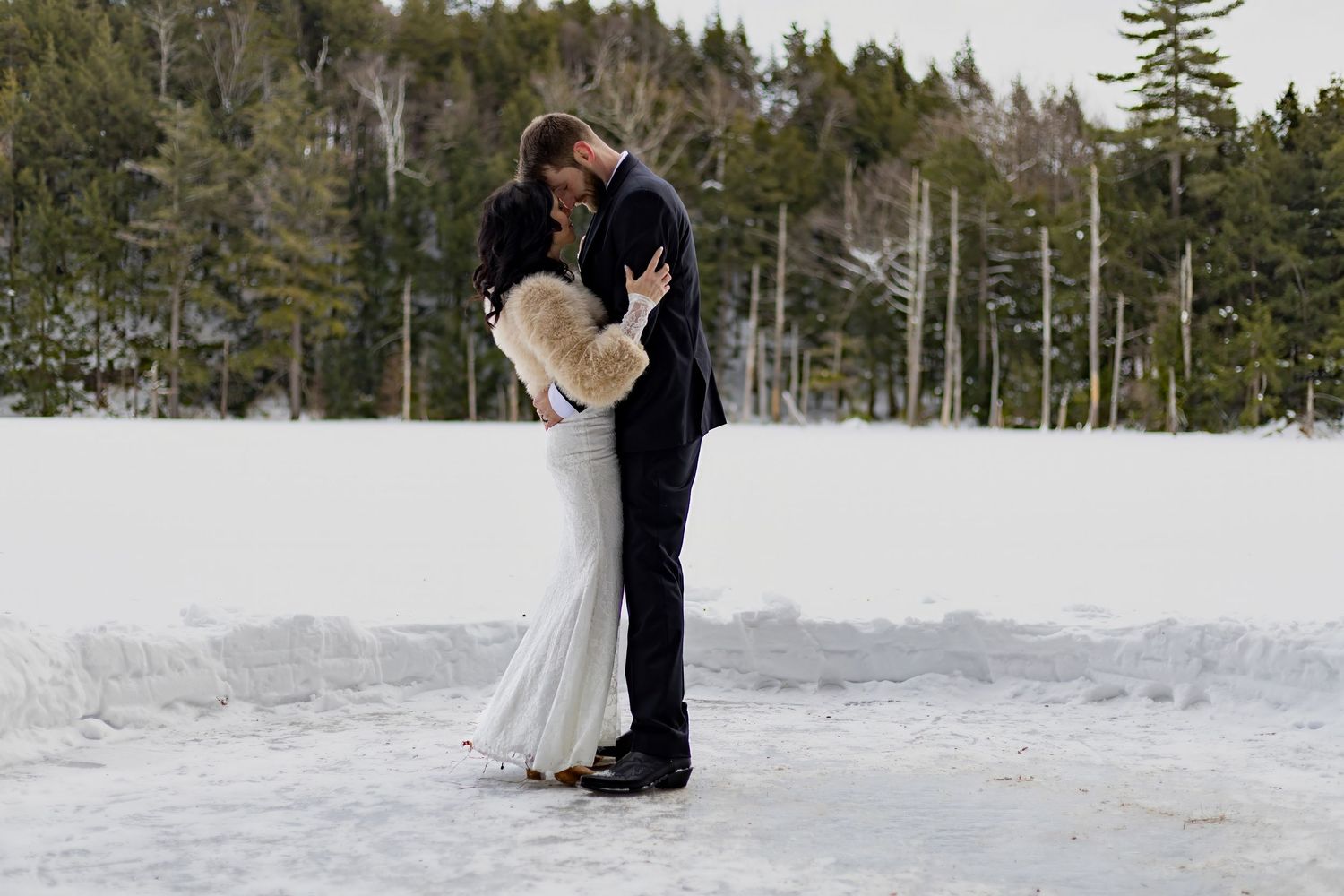 Winter wedding couple embracing in snow-covered forest setting.