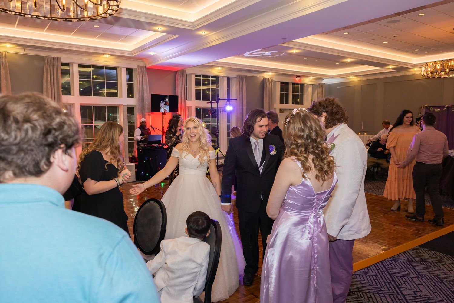 Wedding reception scene with guests dancing under elegant lighting and decor.
