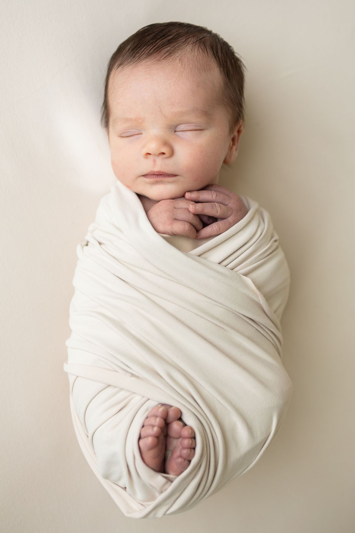 Peaceful newborn baby swaddled in a white wrap, sleeping with tiny hands and feet visible.