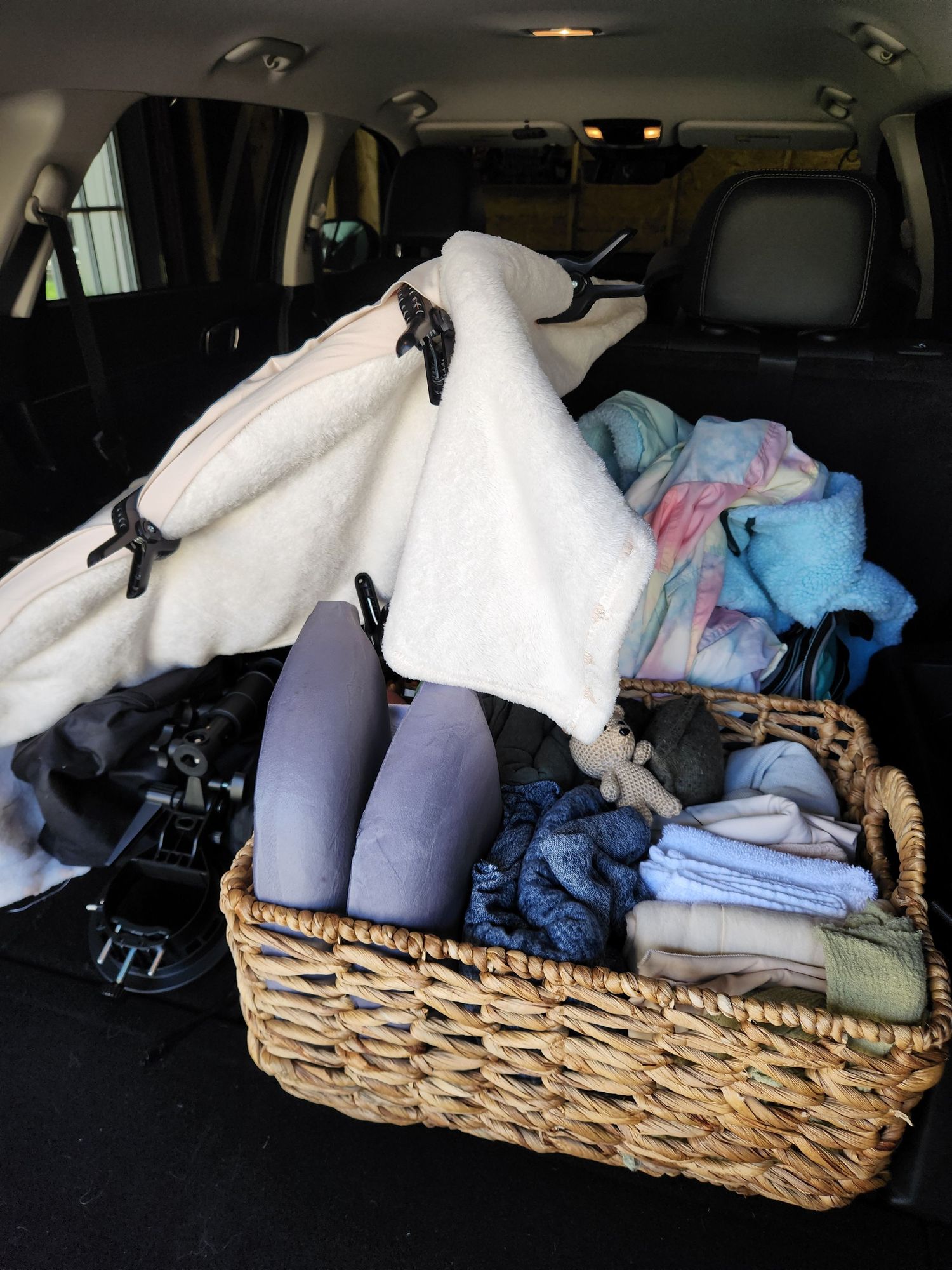 Wicker basket filled with folded towels and linens in the trunk of an SUV with a white blanket draped over items.