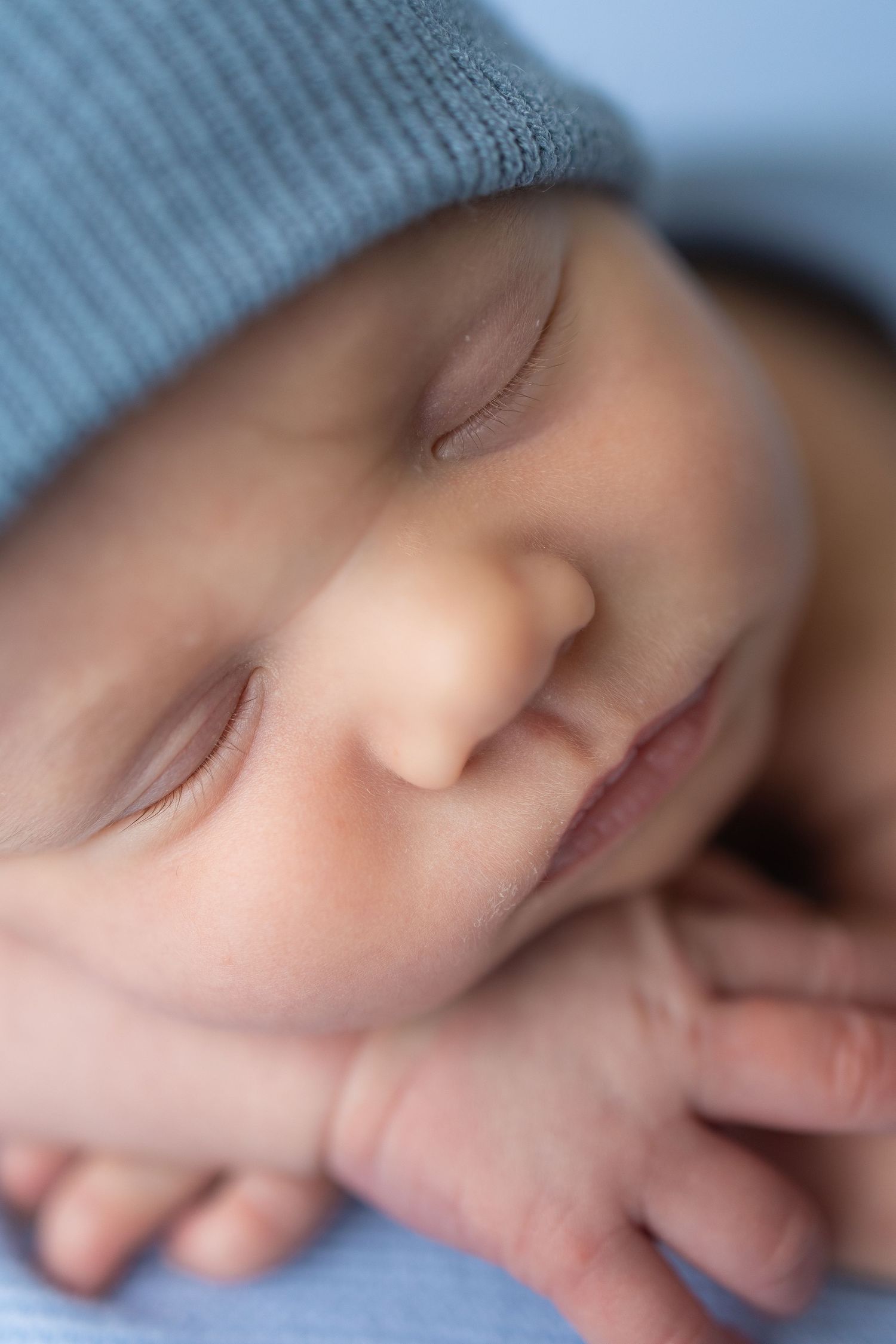 Peaceful newborn baby sleeping soundly, wearing a soft blue knit hat, with tiny hands tucked under cheek.