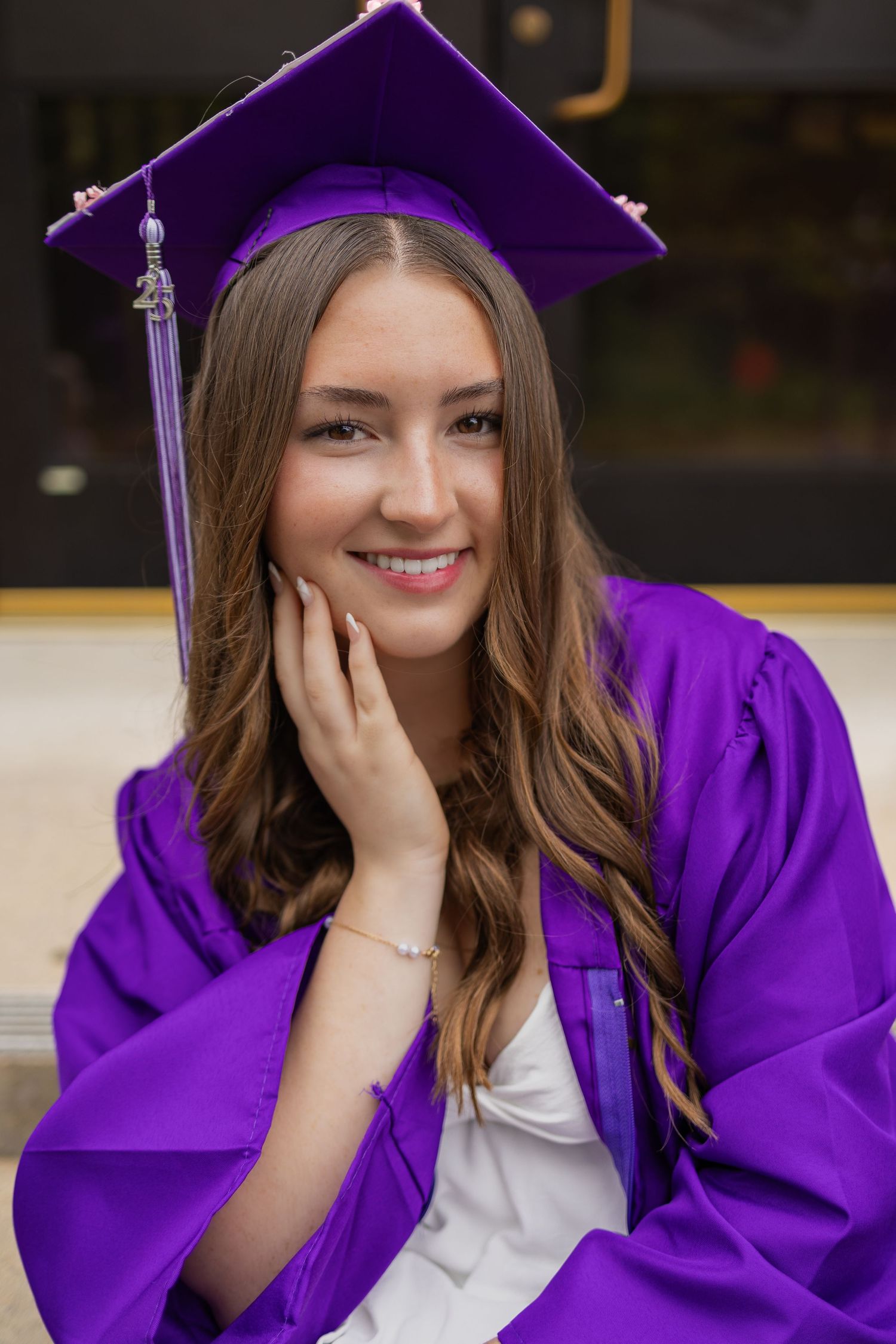 Graduate in purple regalia poses with hand on cheek for graduation photos.