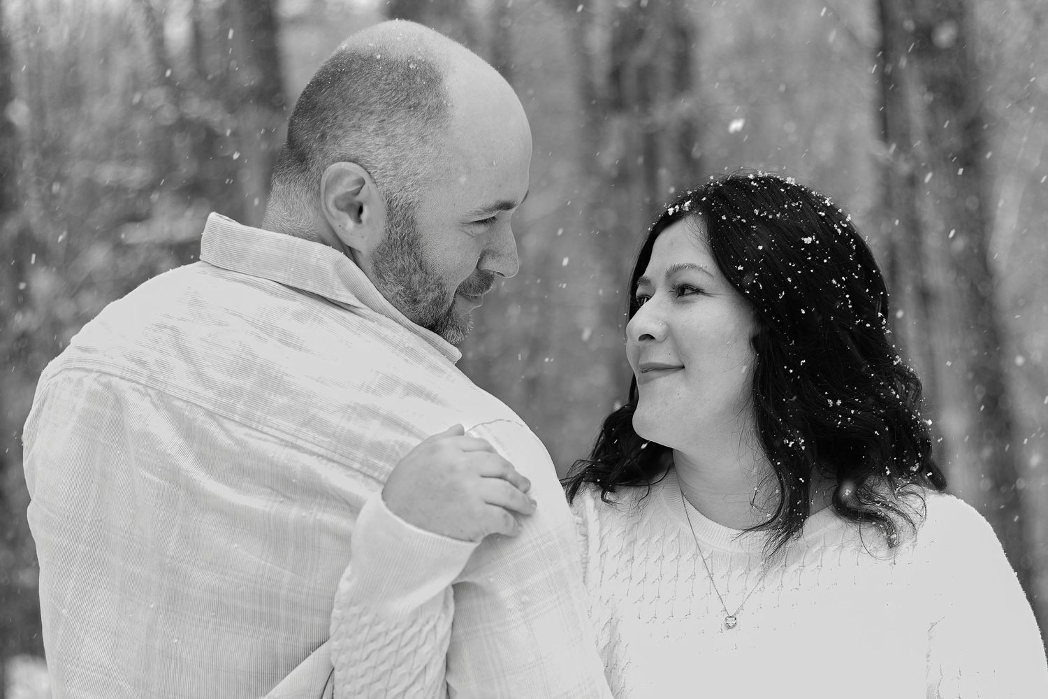 A tender black and white portrait of a couple sharing an intimate moment in the falling snow.