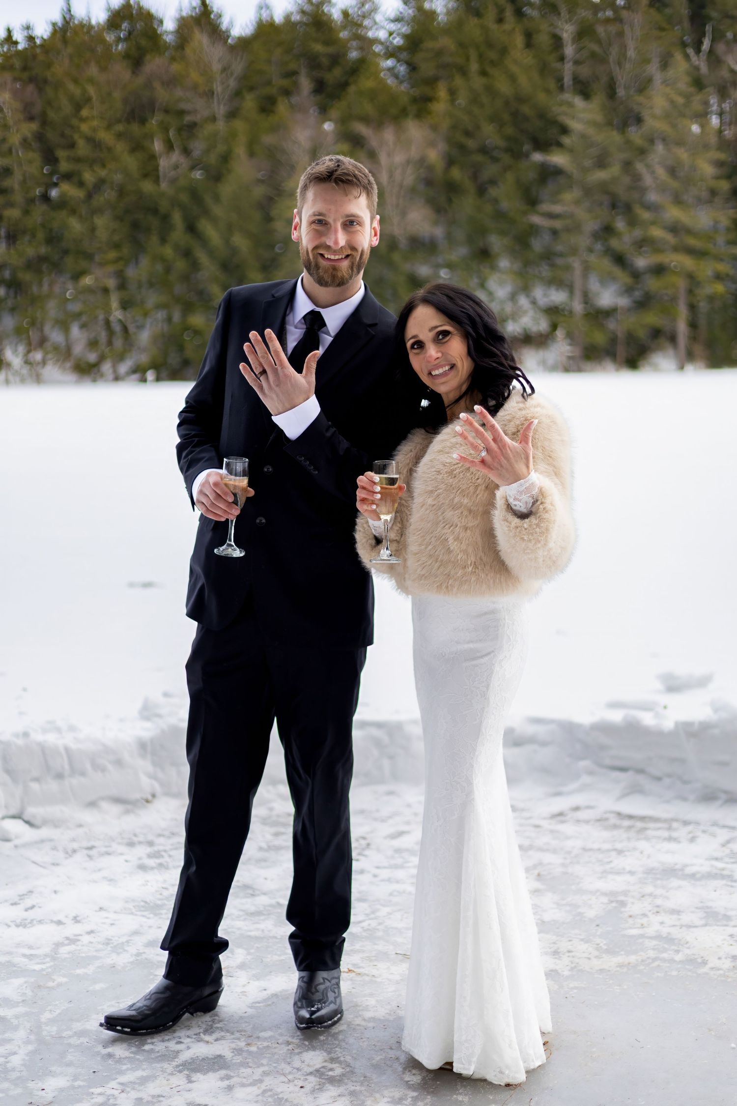 A winter wedding couple shares playful moments in the snow with evergreen trees in the background.