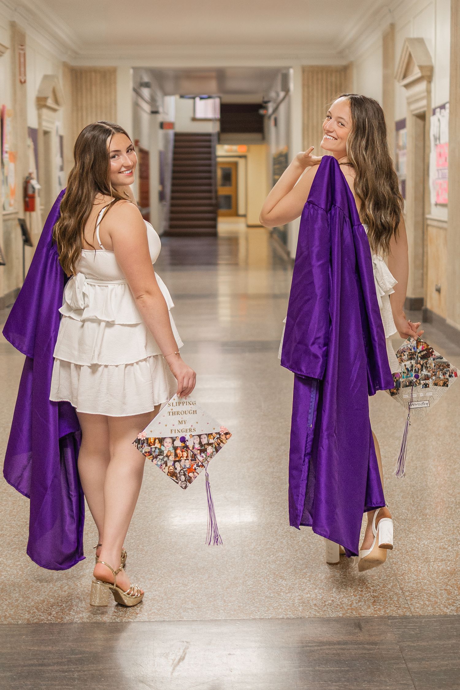 Graduate walks down school hallway carrying decorated cap in white dress.