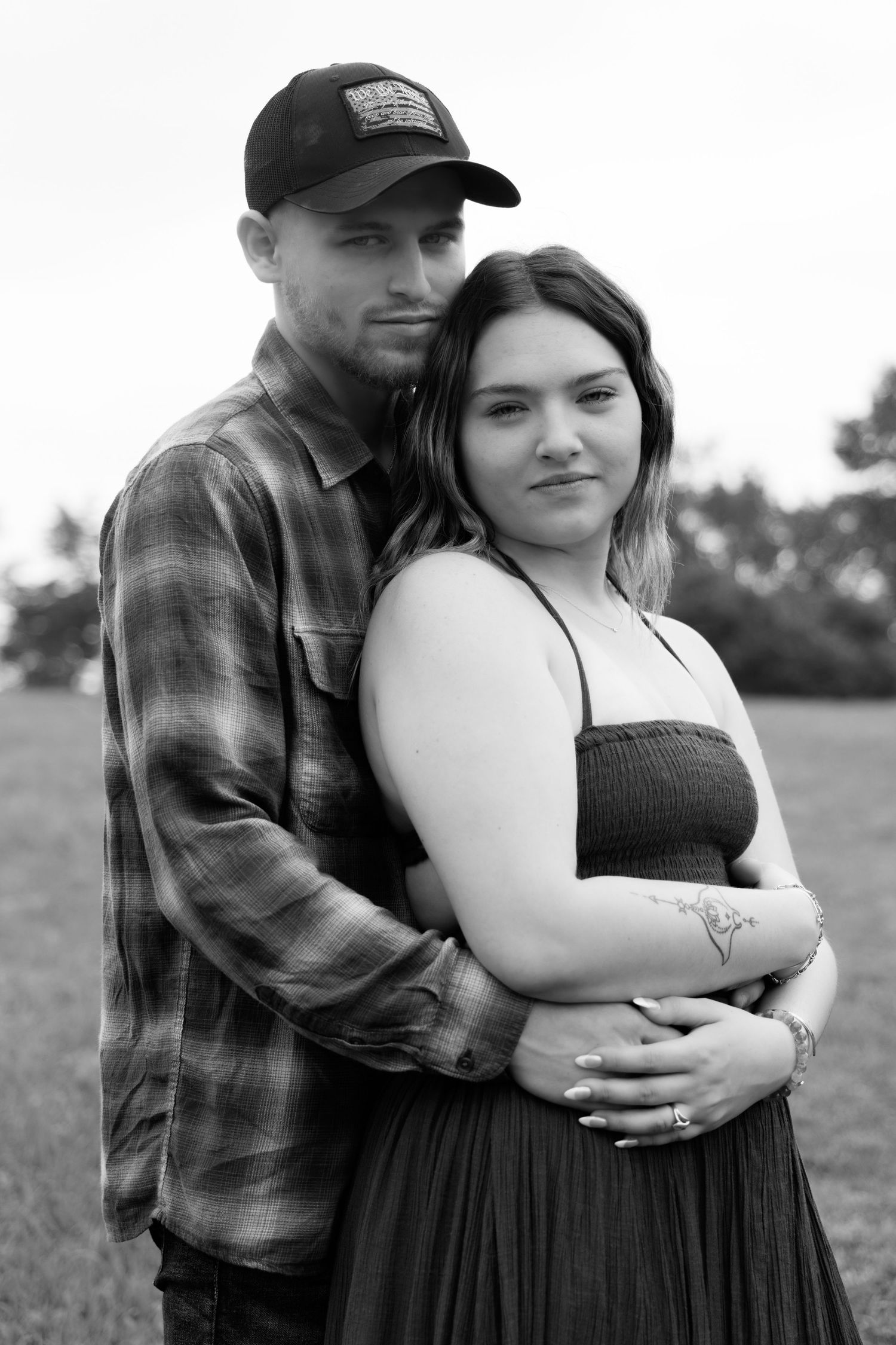 A couple in casual attire shares an intimate embrace in a black and white outdoor portrait.