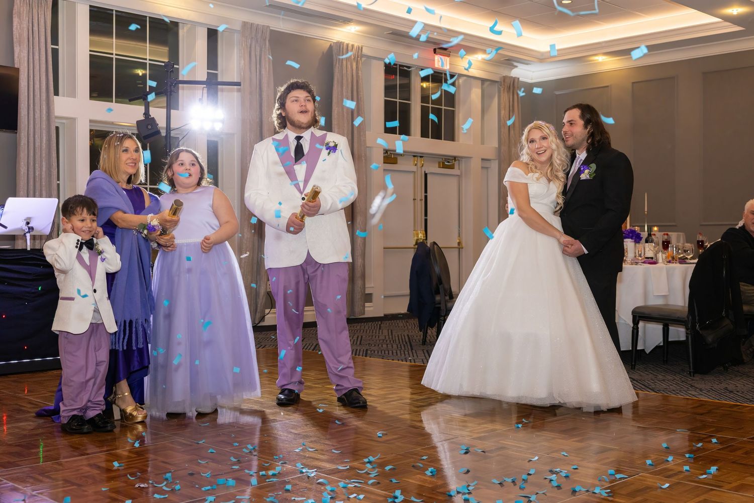 Wedding party members in purple and white dresses dancing during the reception.