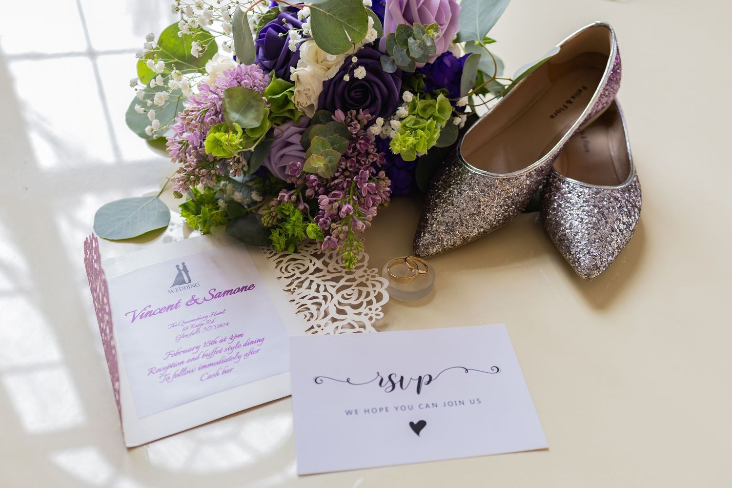 Wedding details including sparkly shoes, floral arrangements, and invitation cards laid out on a white surface.