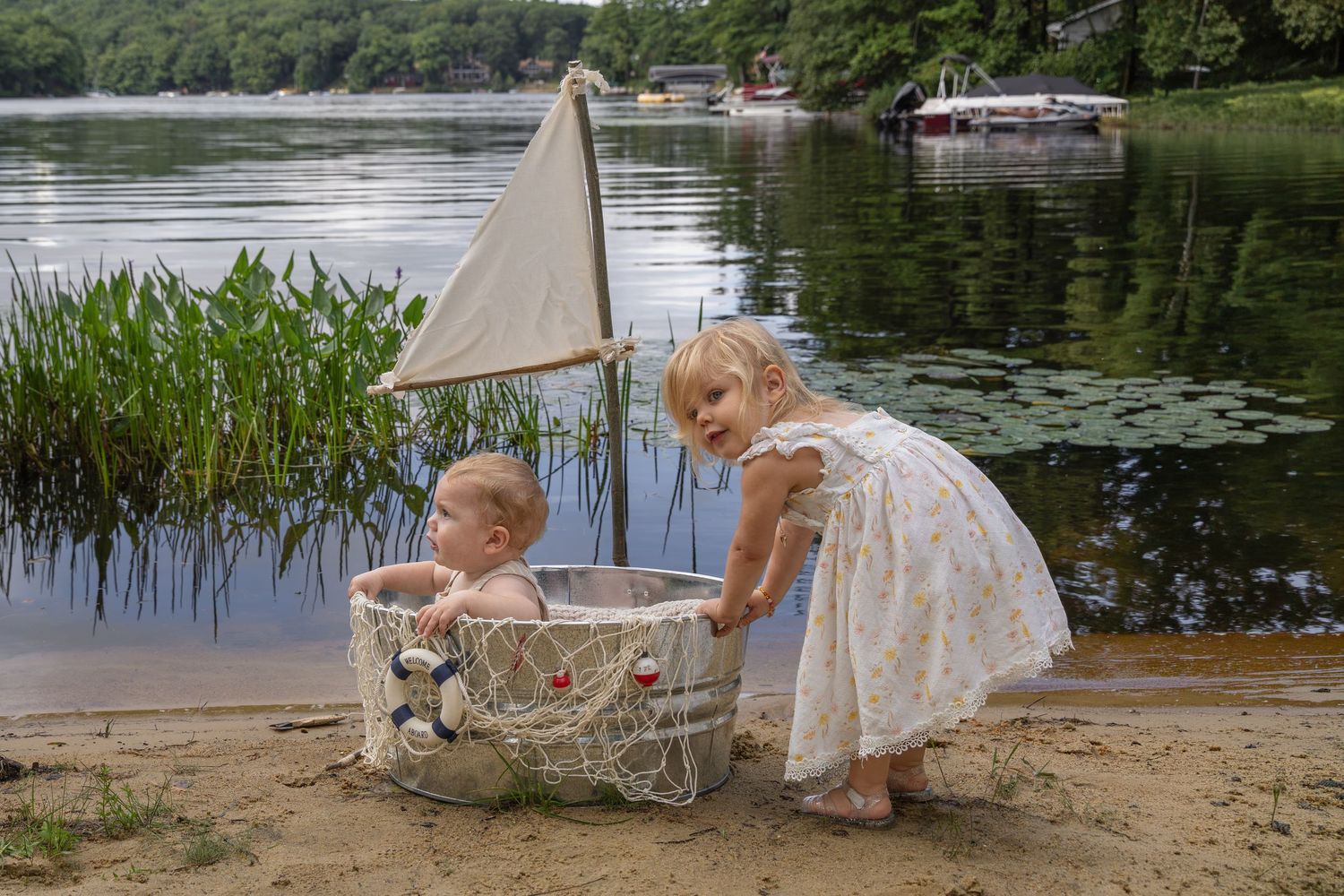 Two young children playing by a lake shore with a toy sailboat basket on sandy beach.