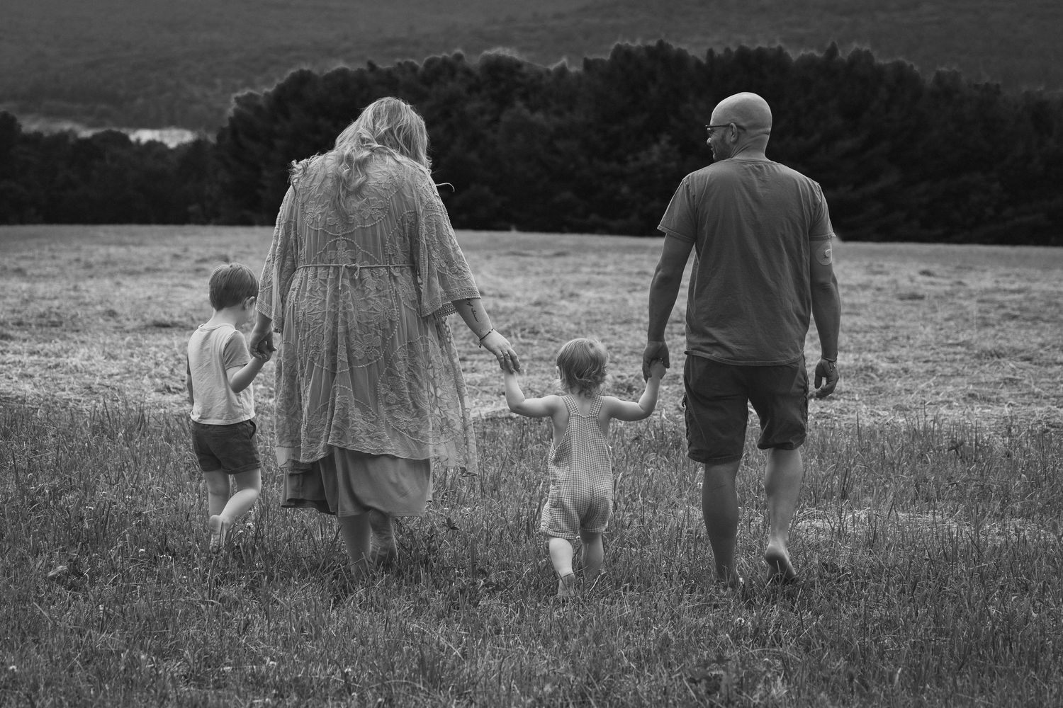 Black and white photo of a family walking through a field, two adults holding hands with two young children.