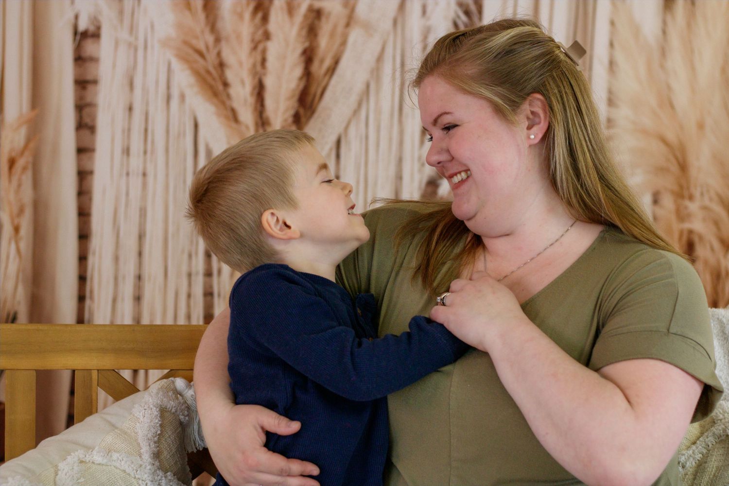 A smiling woman in a green shirt shares a joyful moment with a young boy in a navy shirt.