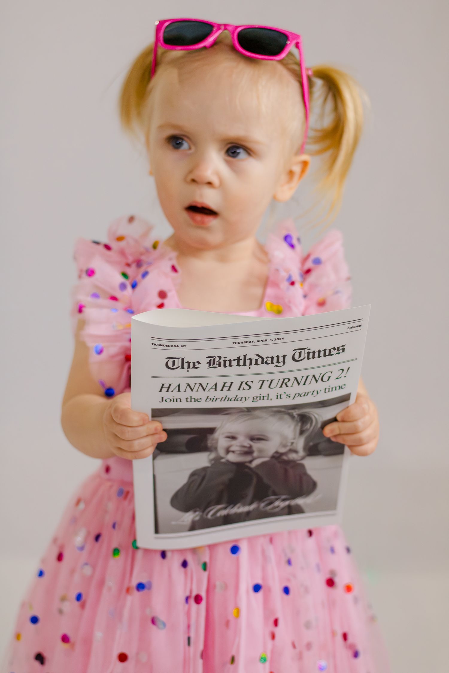 Child in pink polka dot dress holding custom birthday newspaper prop.
