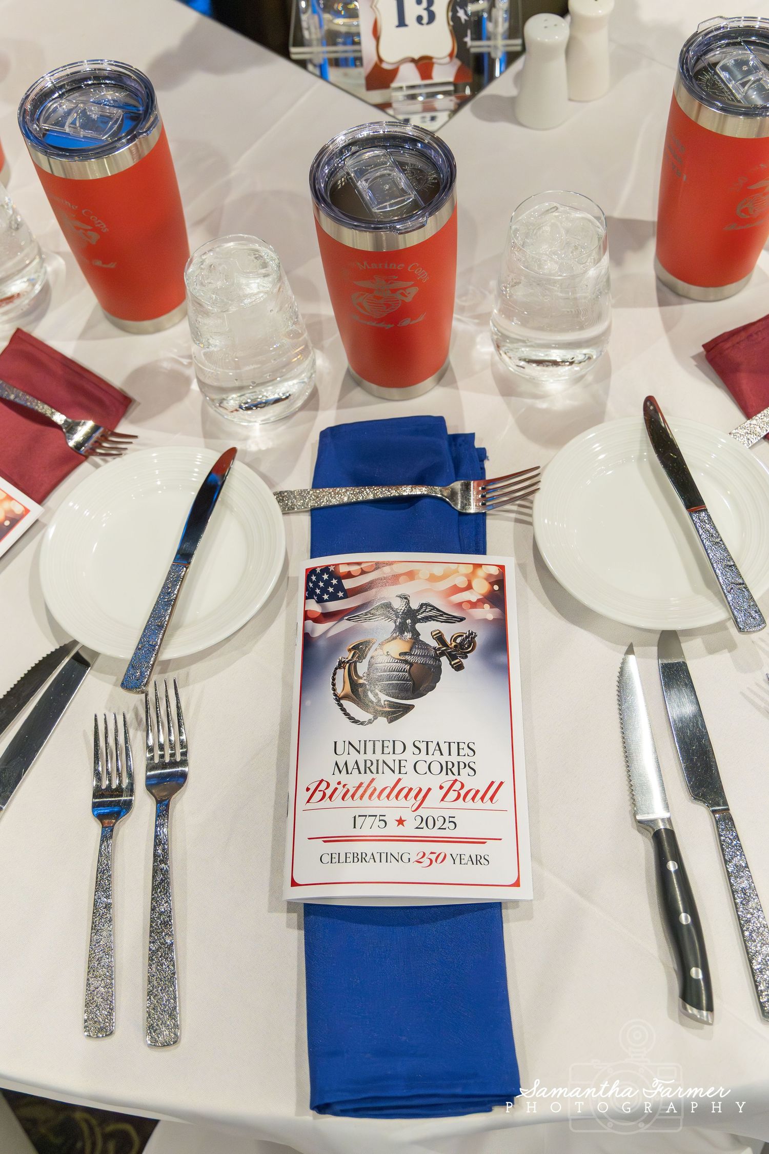 Place settings with blue napkins and United States Marine Corps logo at a formal dinner.