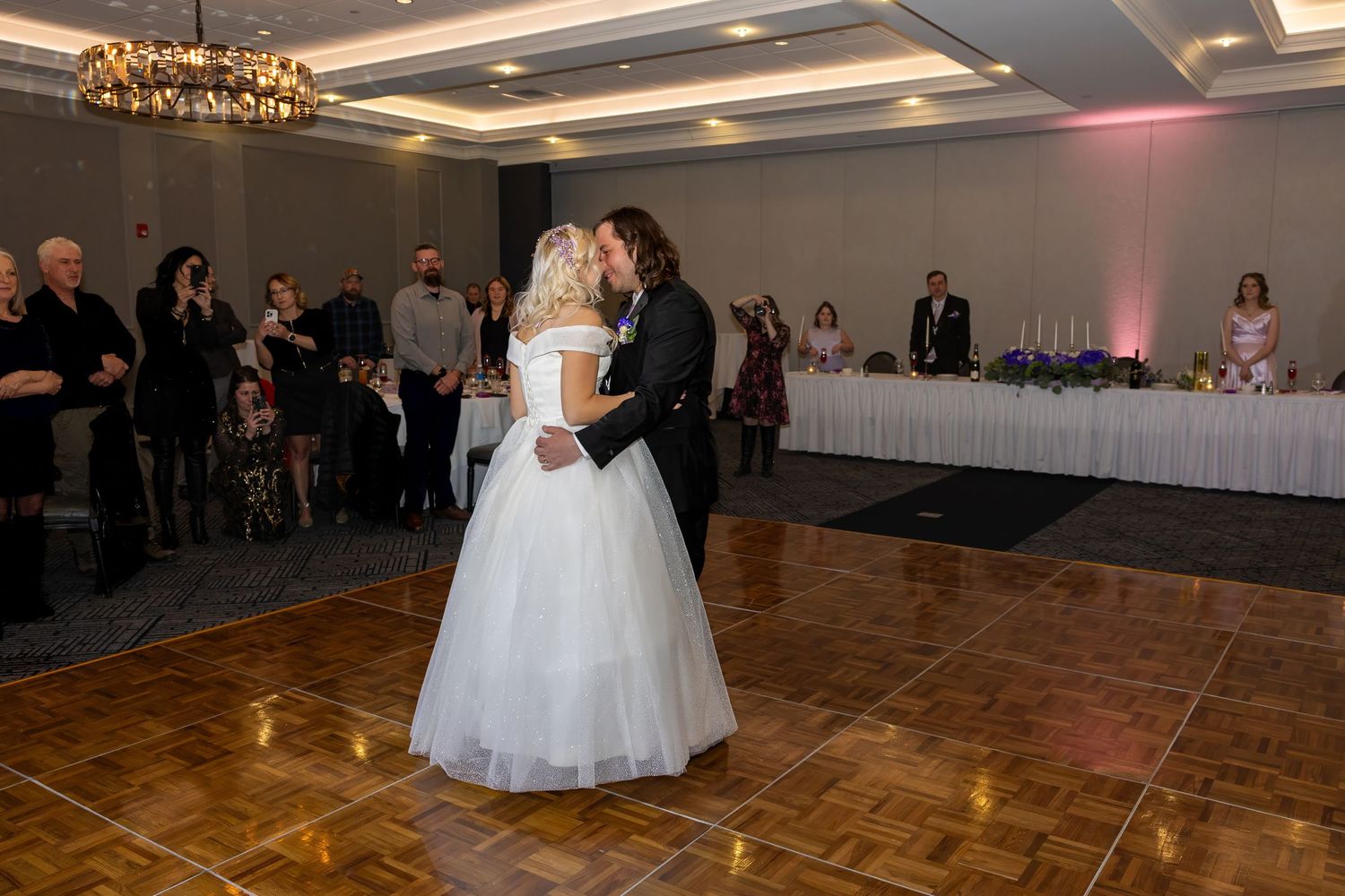 Wedding reception in an elegant ballroom with guests dancing under chandeliers.